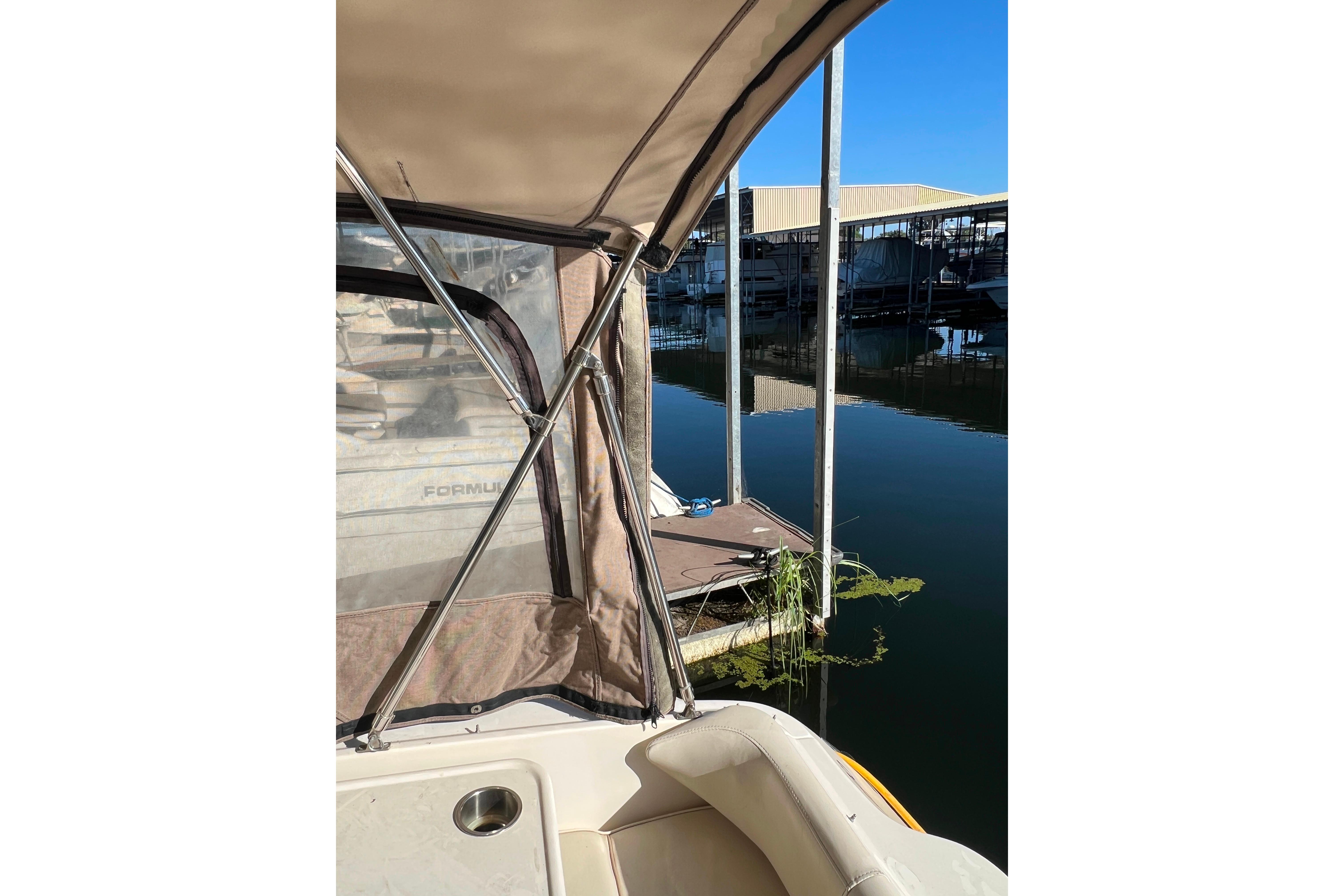 1999 Sea Ray 290 Sundancer at marina, featuring beige canopy and calm water reflection.