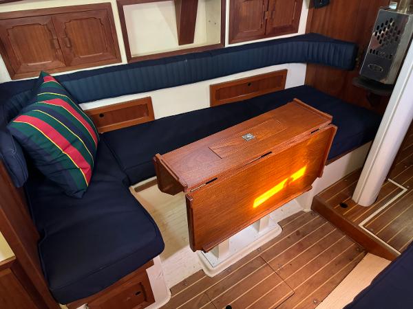 Interior of a 1990 Contessa 32 yacht with wooden table and blue cushions.