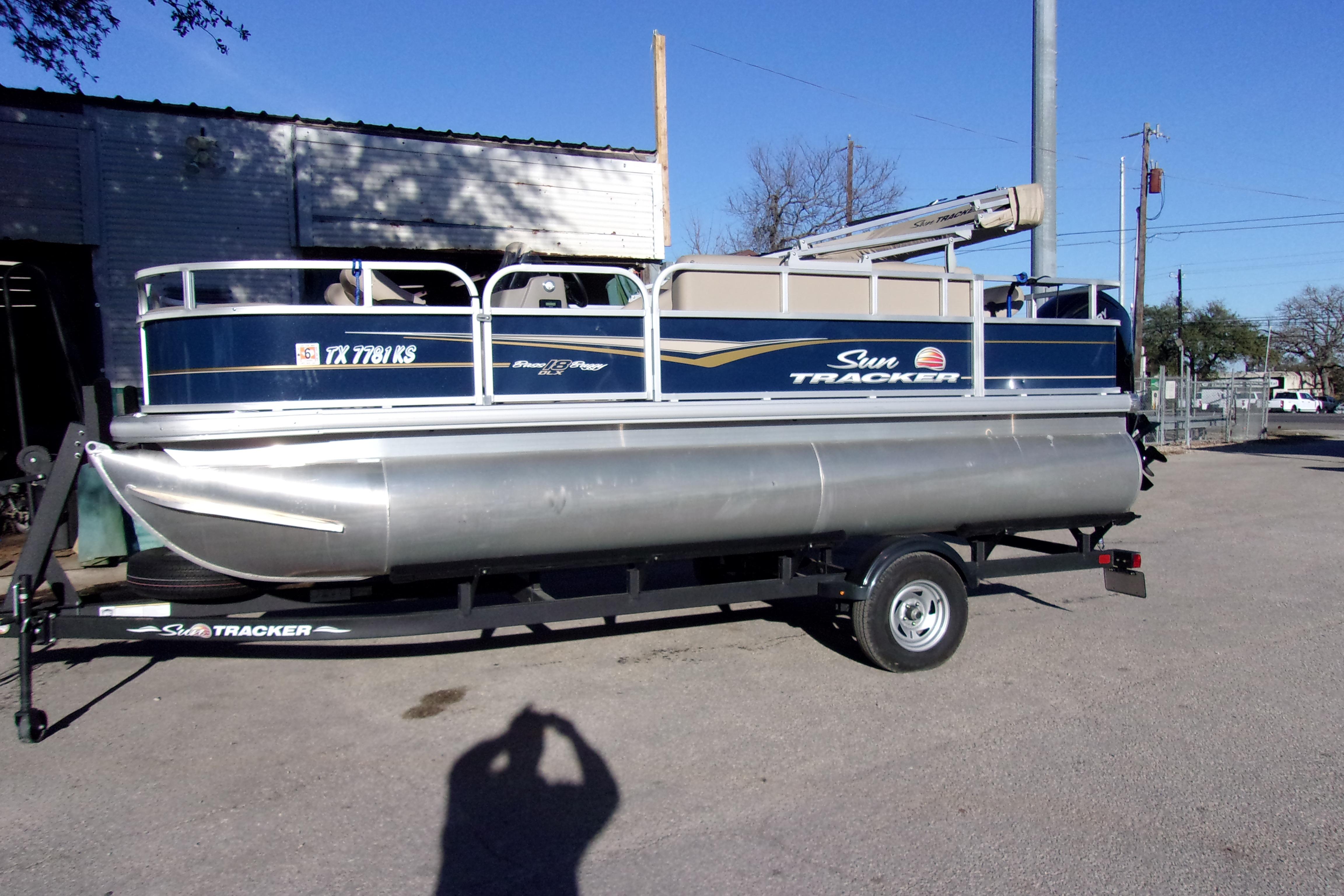 2023 Sun Tracker Bass Buggy 18 DLX pontoon boat on trailer, parked outdoors.