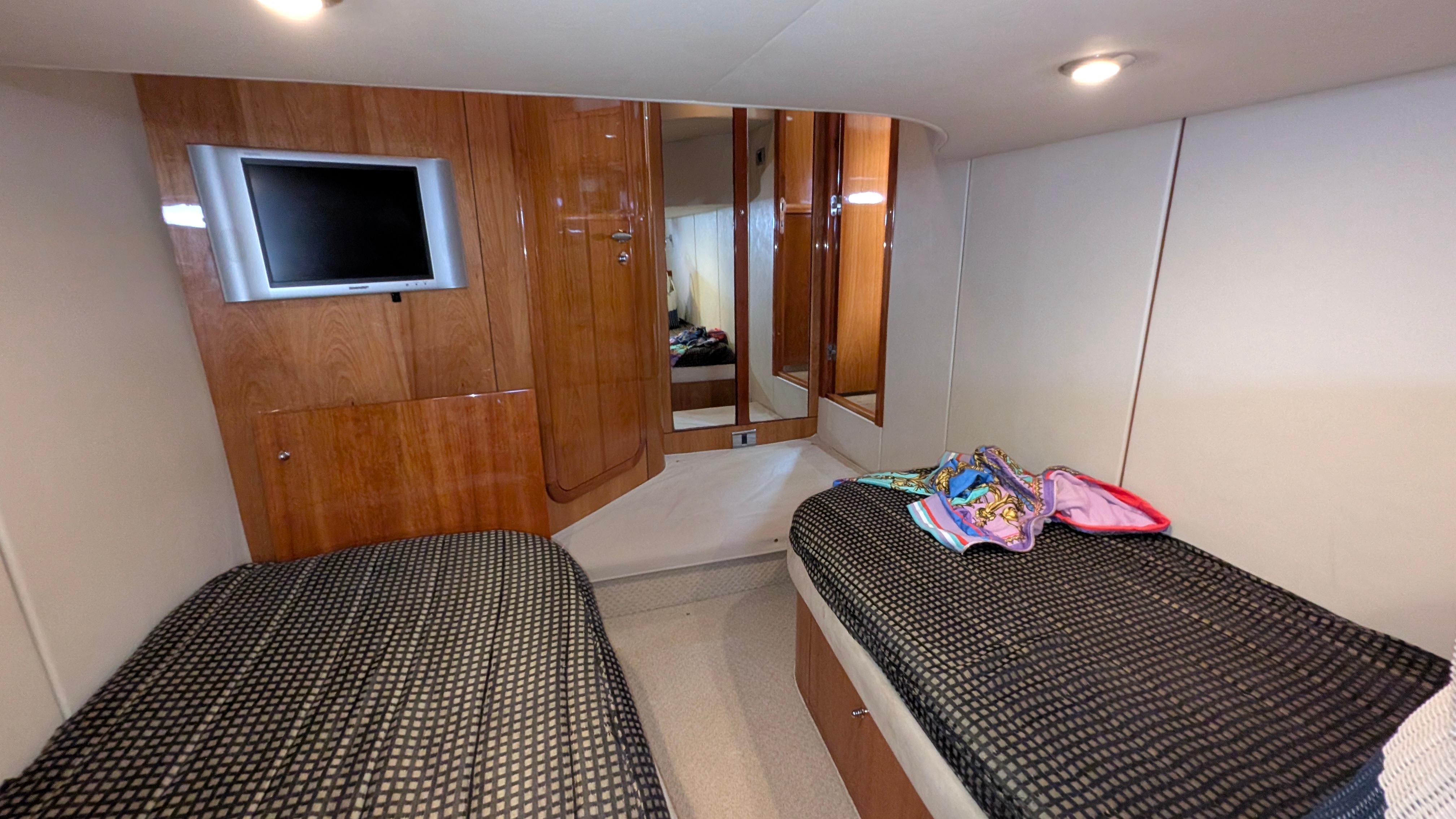 2004 Sunseeker Portofino cabin with twin beds, wooden paneling, and a wall-mounted TV.