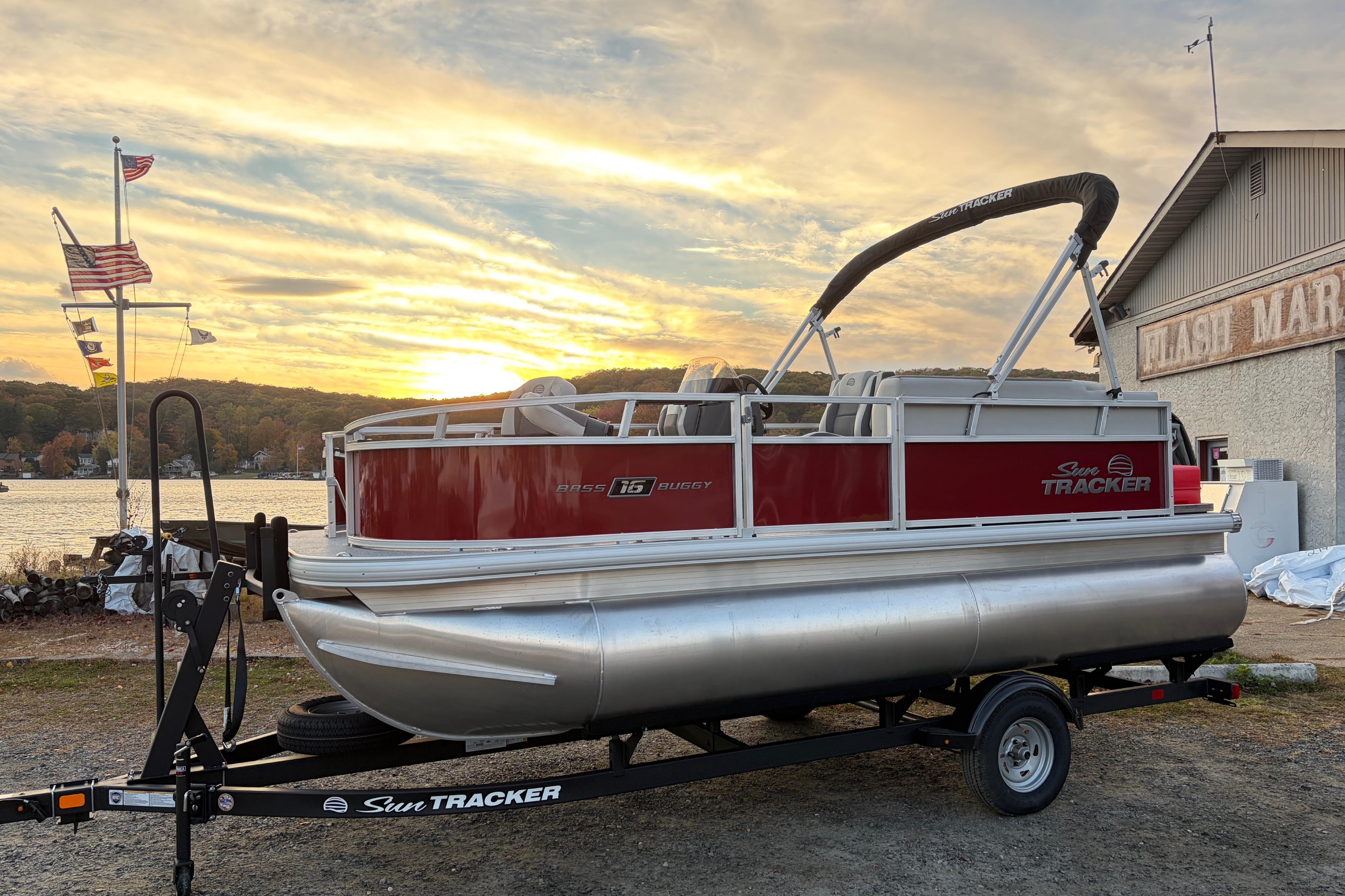 2026 Sun Tracker Bass Buggy 16 XL Select pontoon boat at sunset by a marina.