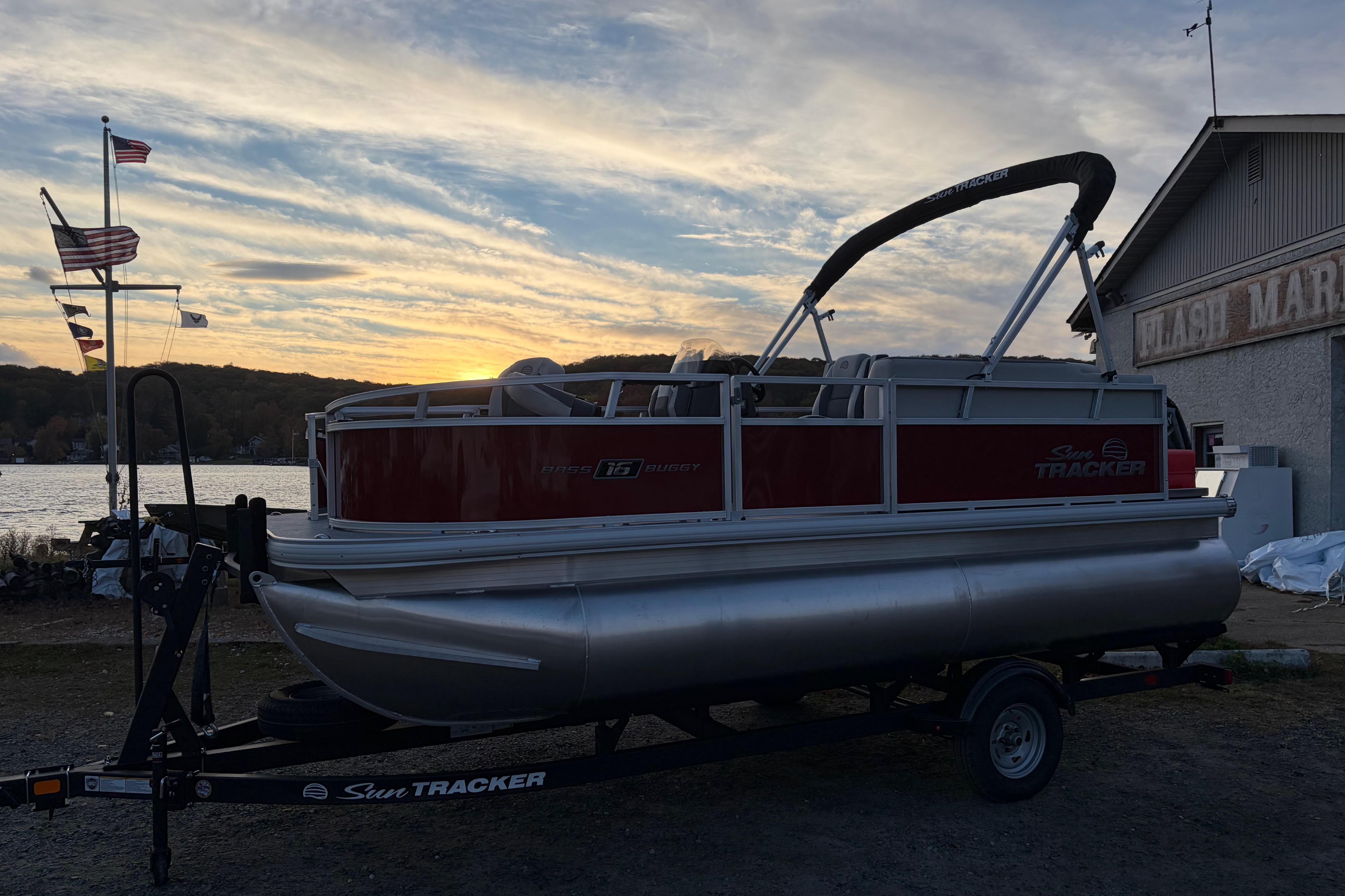 2026 Sun Tracker Bass Buggy 16 XL Select pontoon boat at sunset by a lake.