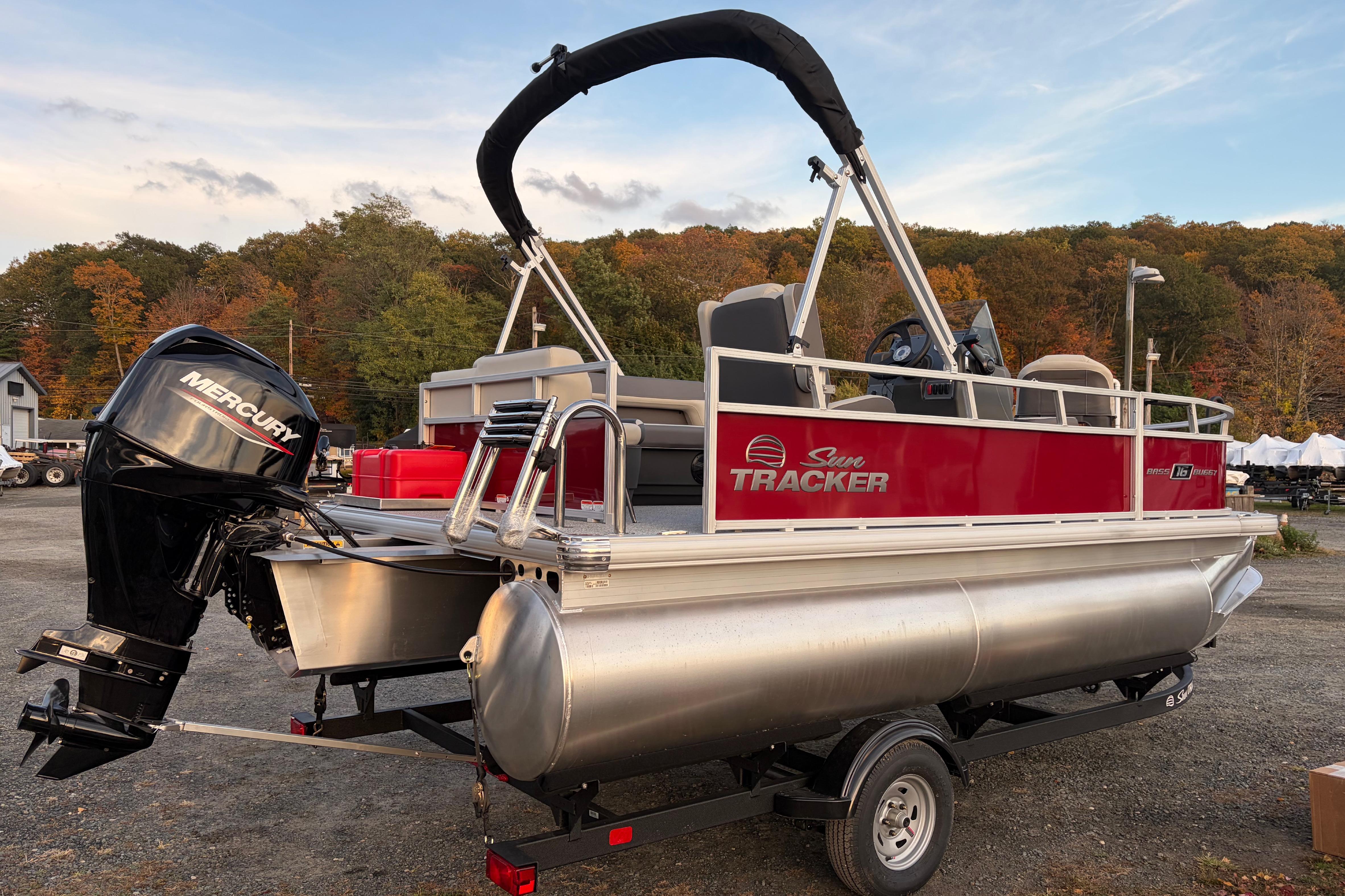 2026 Sun Tracker Bass Buggy 16 XL Select pontoon boat with Mercury engine, parked outdoors.