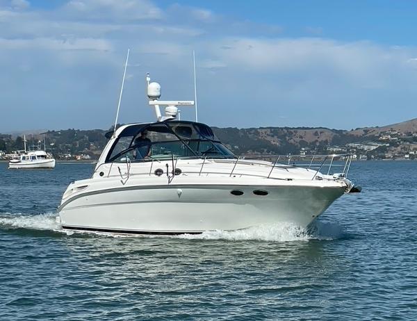 2000 Sea Ray 380 Sundancer cruising on a calm lake under a clear blue sky.