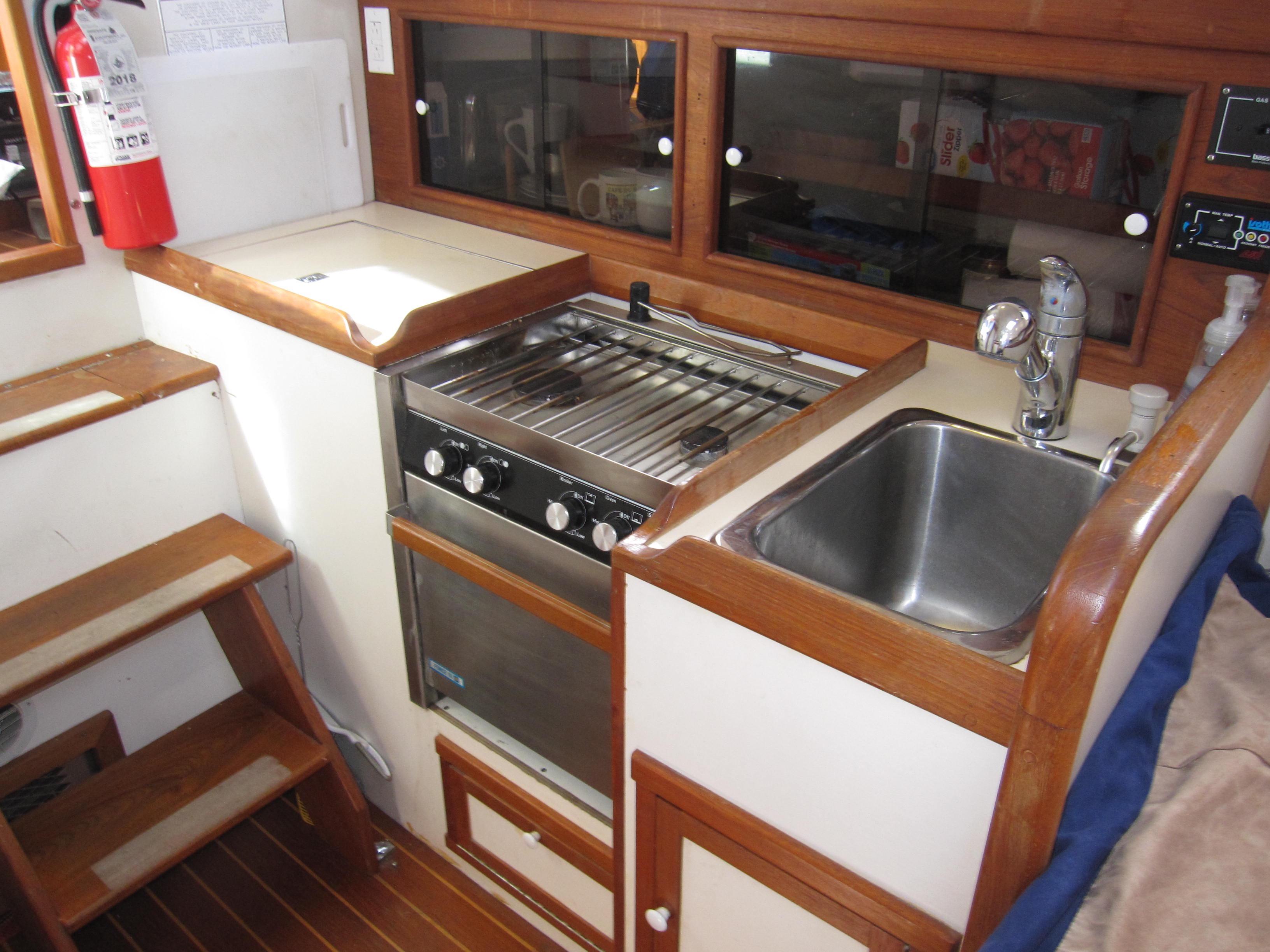 Compact kitchen area in 1990 Blue Seas 31 Hardtop Cruiser with stove, sink, and wooden cabinetry.