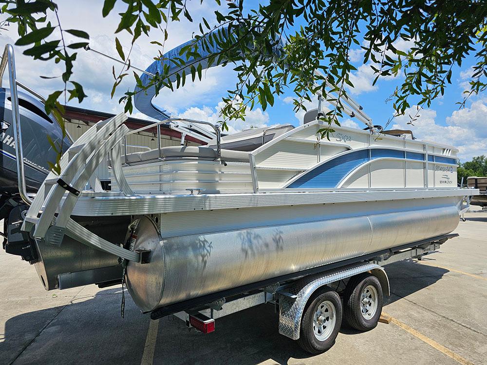 2022 Bennington 22 SXSB pontoon boat on trailer under leafy branches.