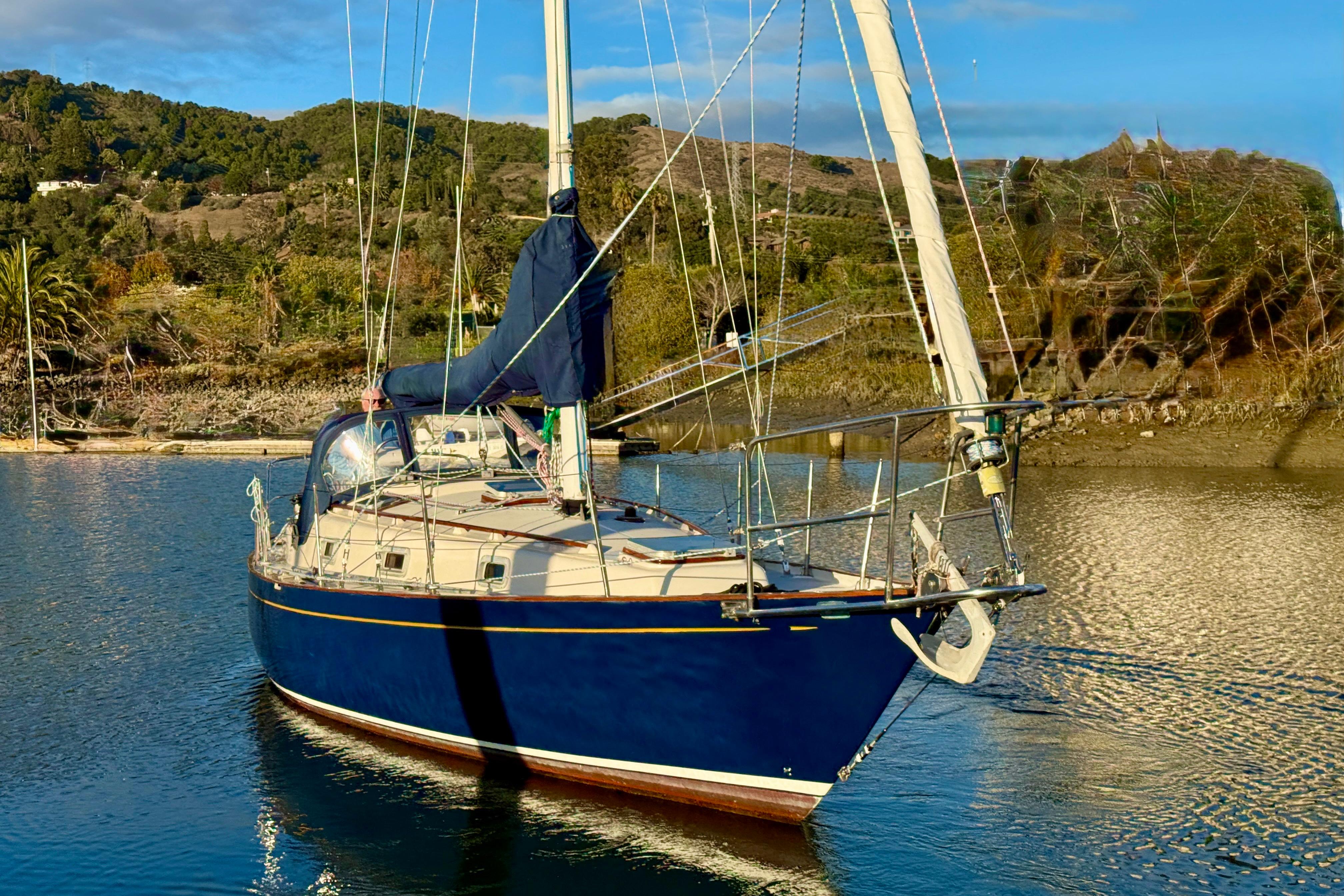1990 Contessa 32 sailboat on calm water with scenic hillside background.
