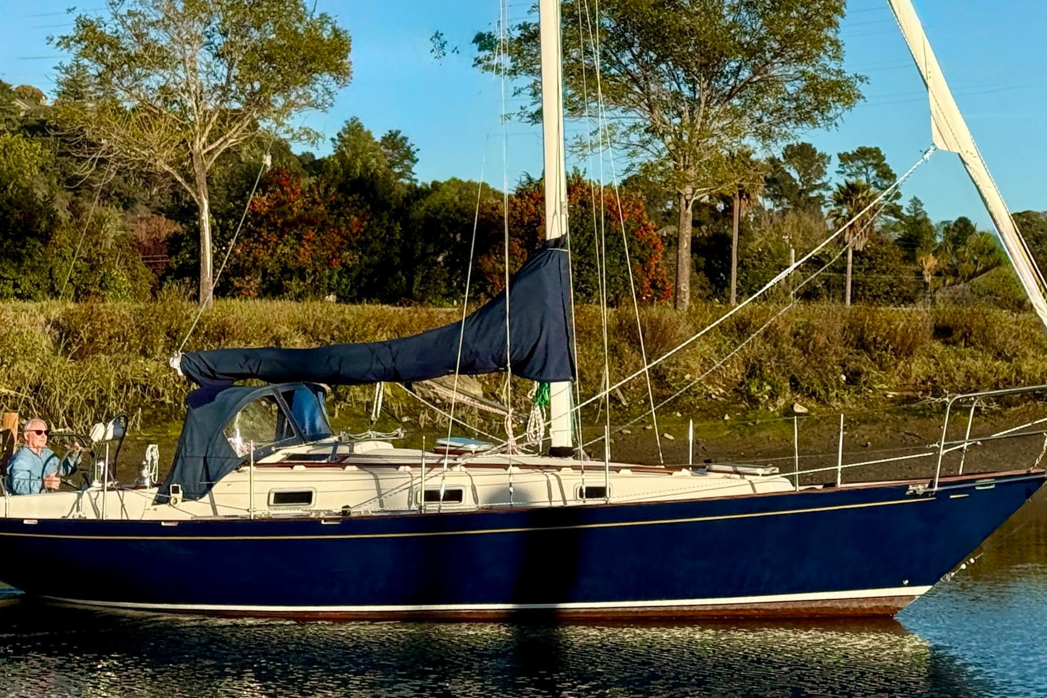Sailboat Contessa 32, 1990 model, anchored near lush greenery and calm waters.