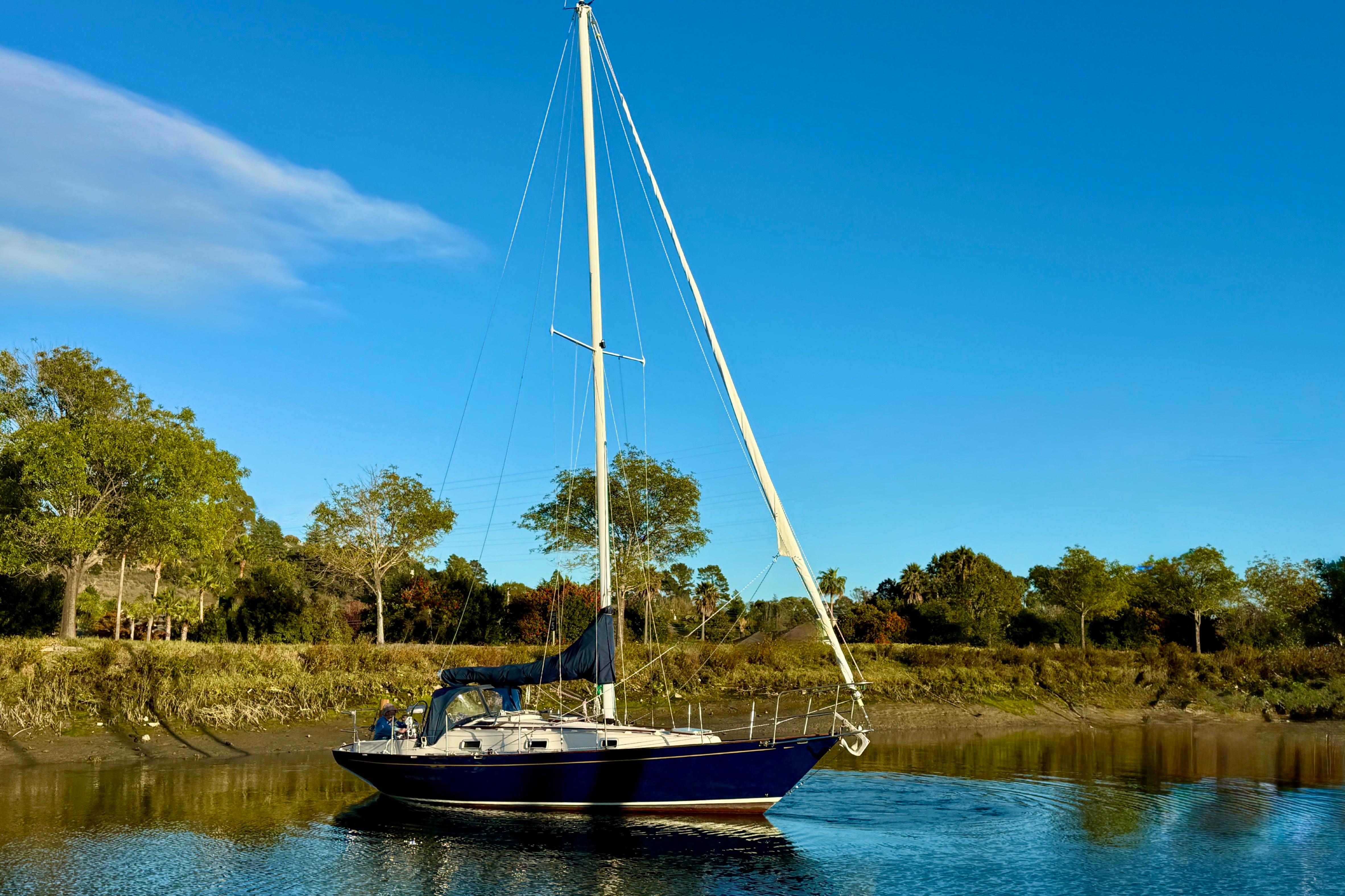 Sailboat Contessa 32 from 1990 on calm water, surrounded by lush greenery.