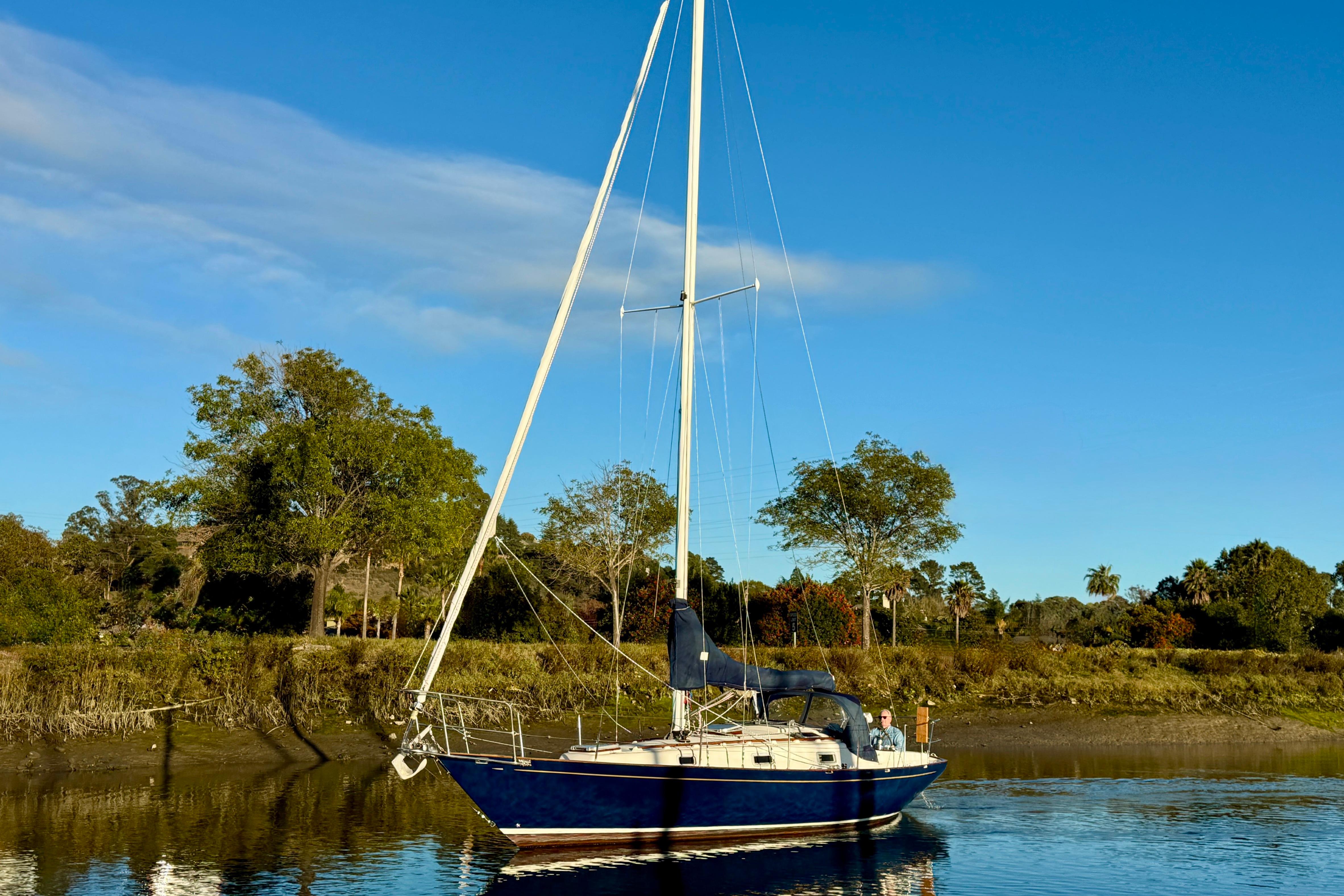 Sailboat Contessa 32 from 1990 on calm water with trees in the background.