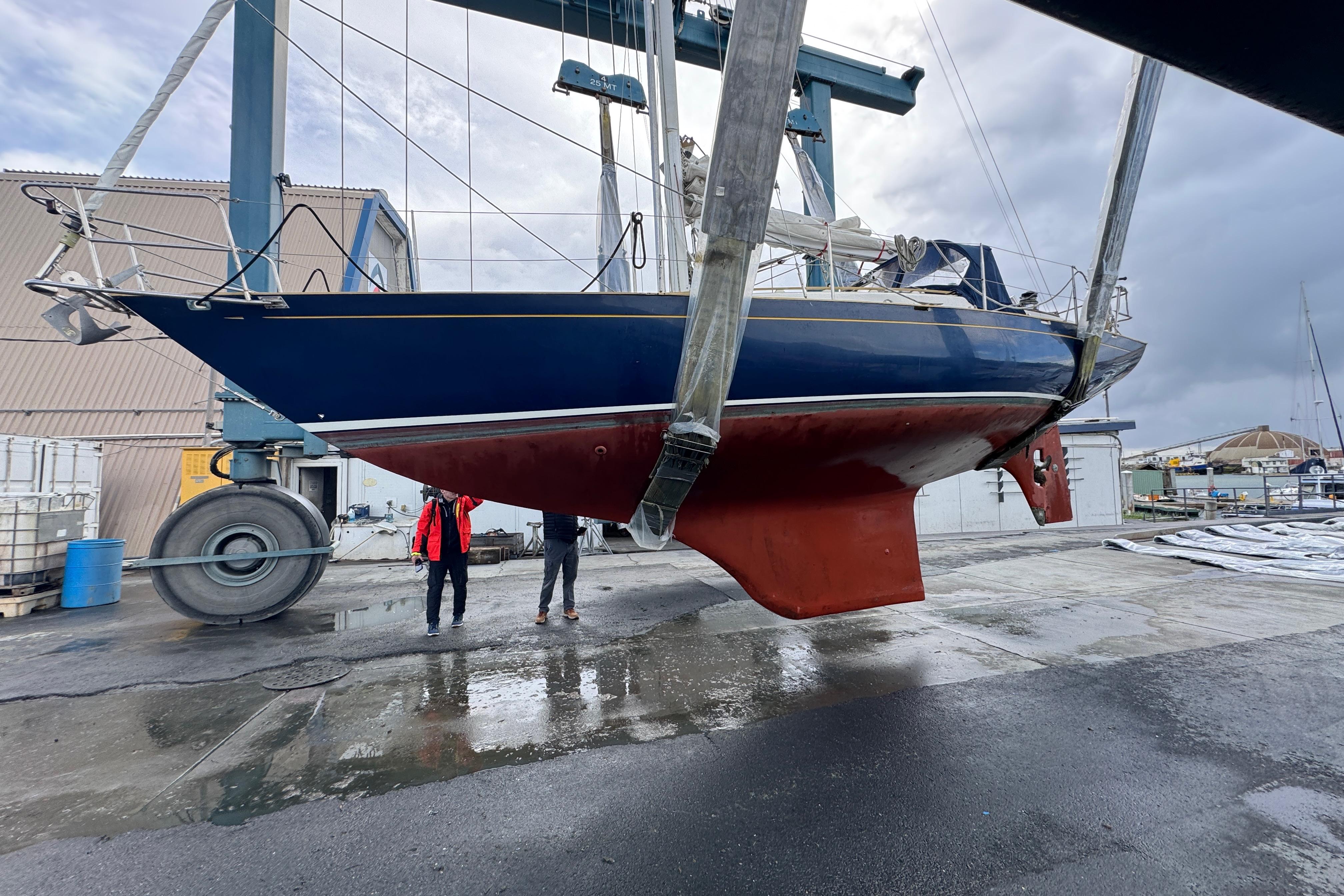 1990 Contessa 32 sailboat lifted in shipyard, blue hull, red keel, overcast sky.