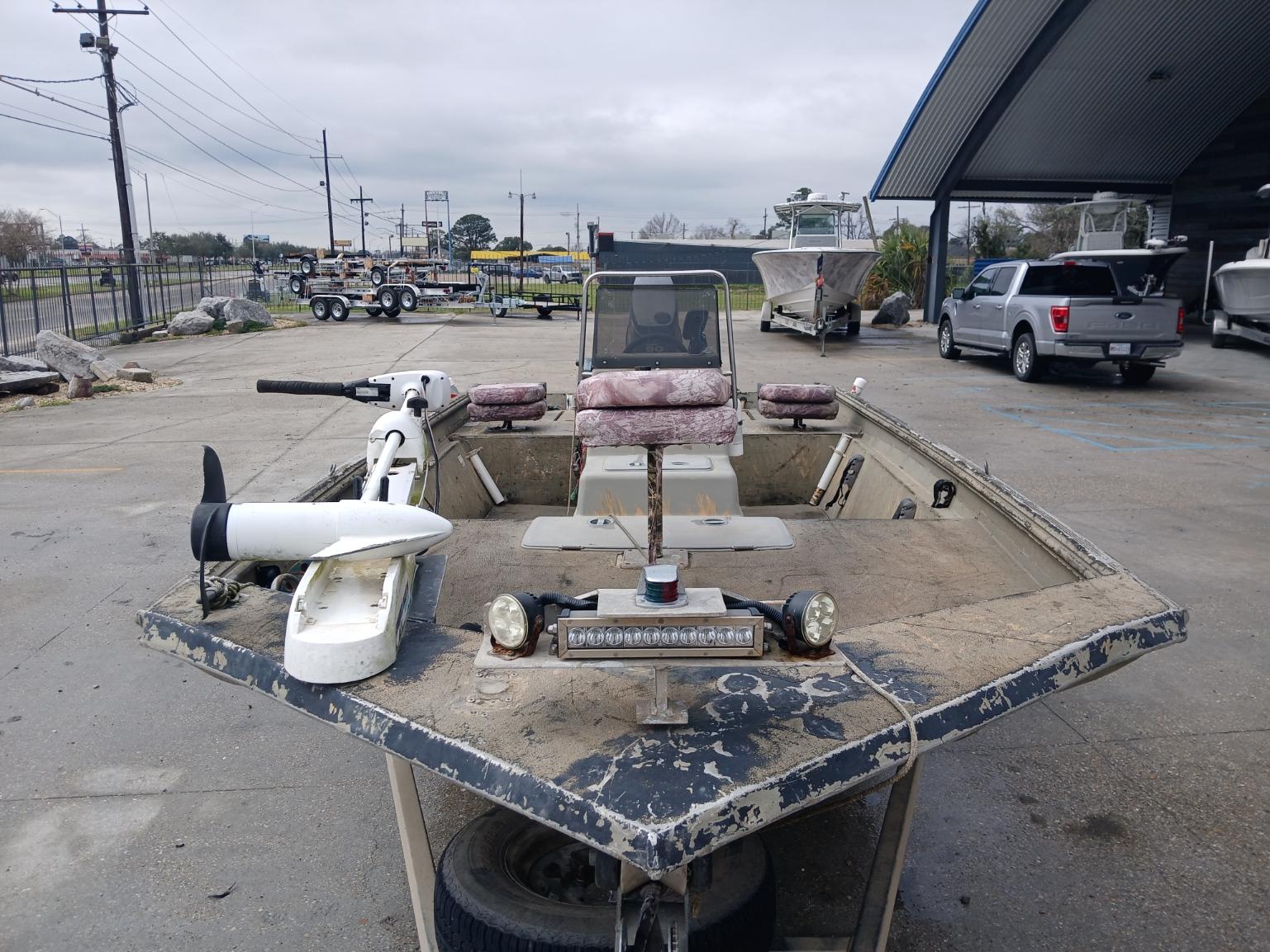 2004 Xpress 18 boat with trolling motor, parked outdoors on a cloudy day.