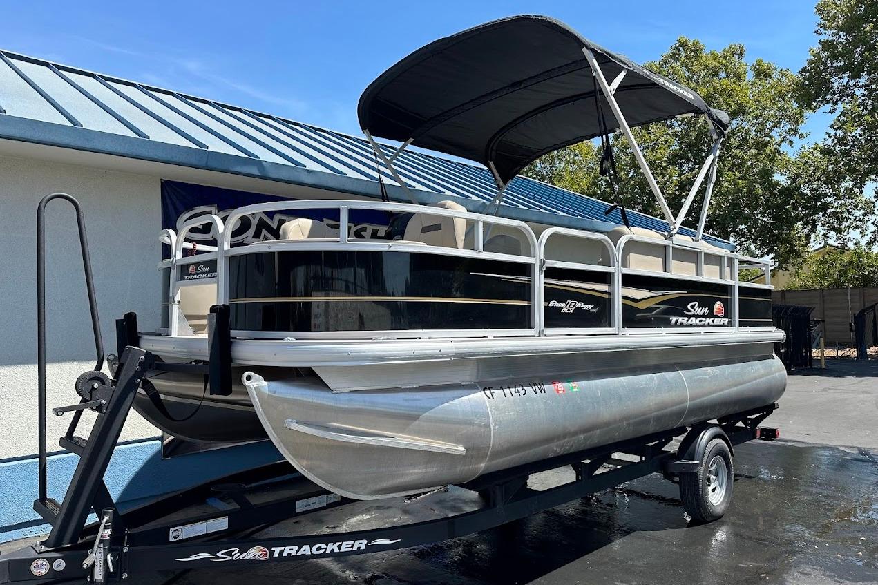 2022 Sun Tracker Bass Buggy 18 DLX pontoon boat on trailer, parked outdoors.