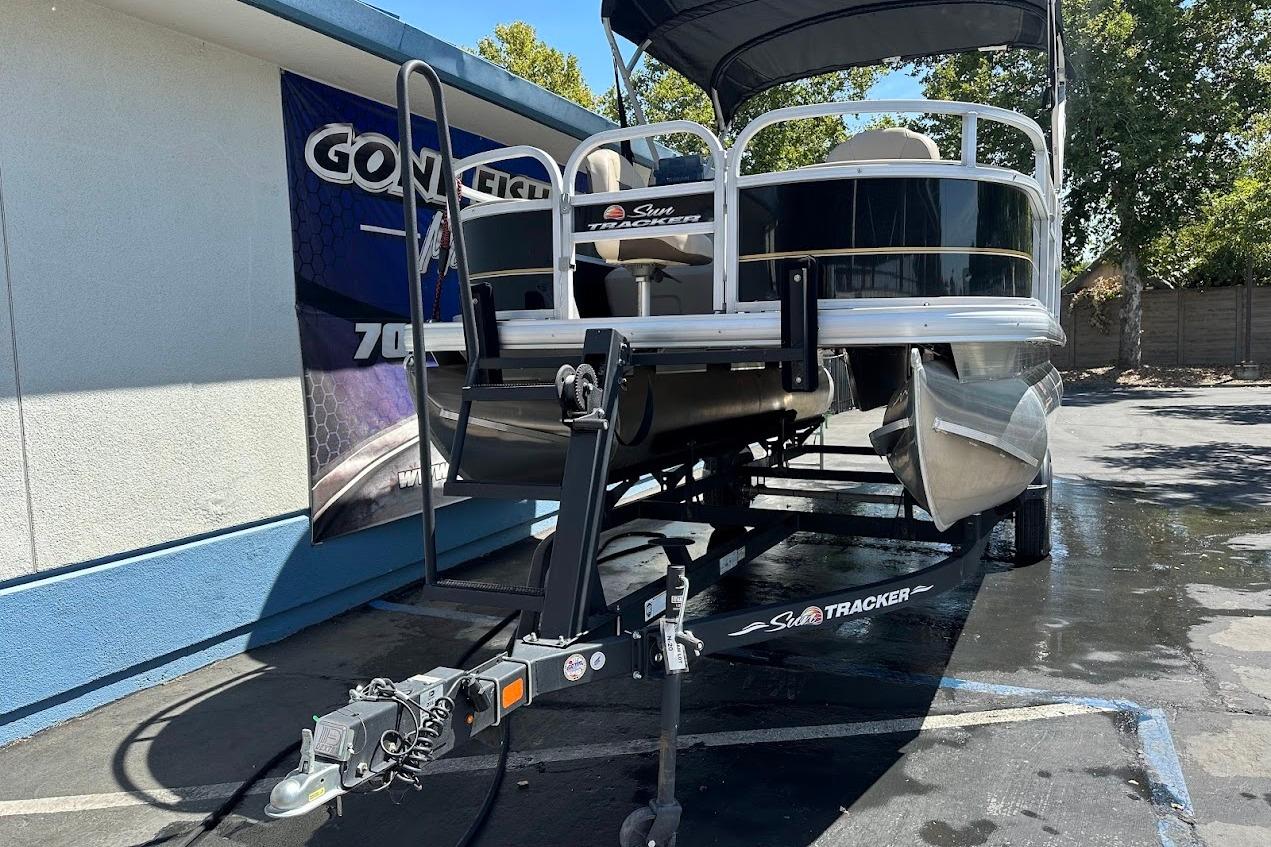 2022 Sun Tracker Bass Buggy 18 DLX pontoon boat on trailer, parked outdoors.