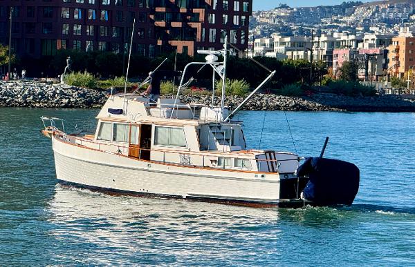 1979 Grand Banks Classic yacht cruising near urban waterfront.