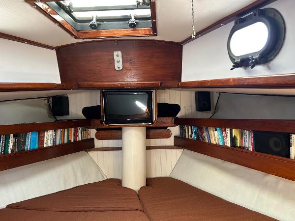 Cozy 1975 Salar 40 yacht cabin with bookshelves, TV, and brown cushions.