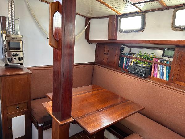 Cozy interior of 1975 Salar 40 sailboat with wooden dining area and bookshelf.