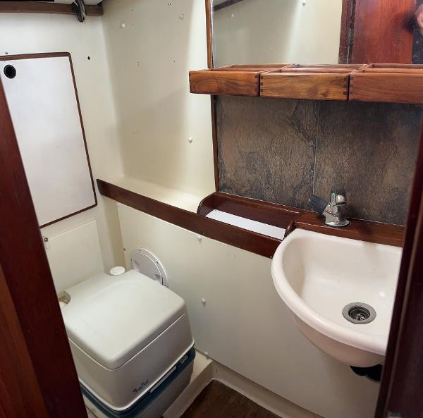 Compact bathroom in a 1975 Salar 40 boat, featuring a sink and portable toilet.