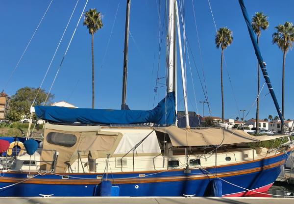 1975 Salar 40 sailboat docked, blue hull, beige canopy, palm trees in background.