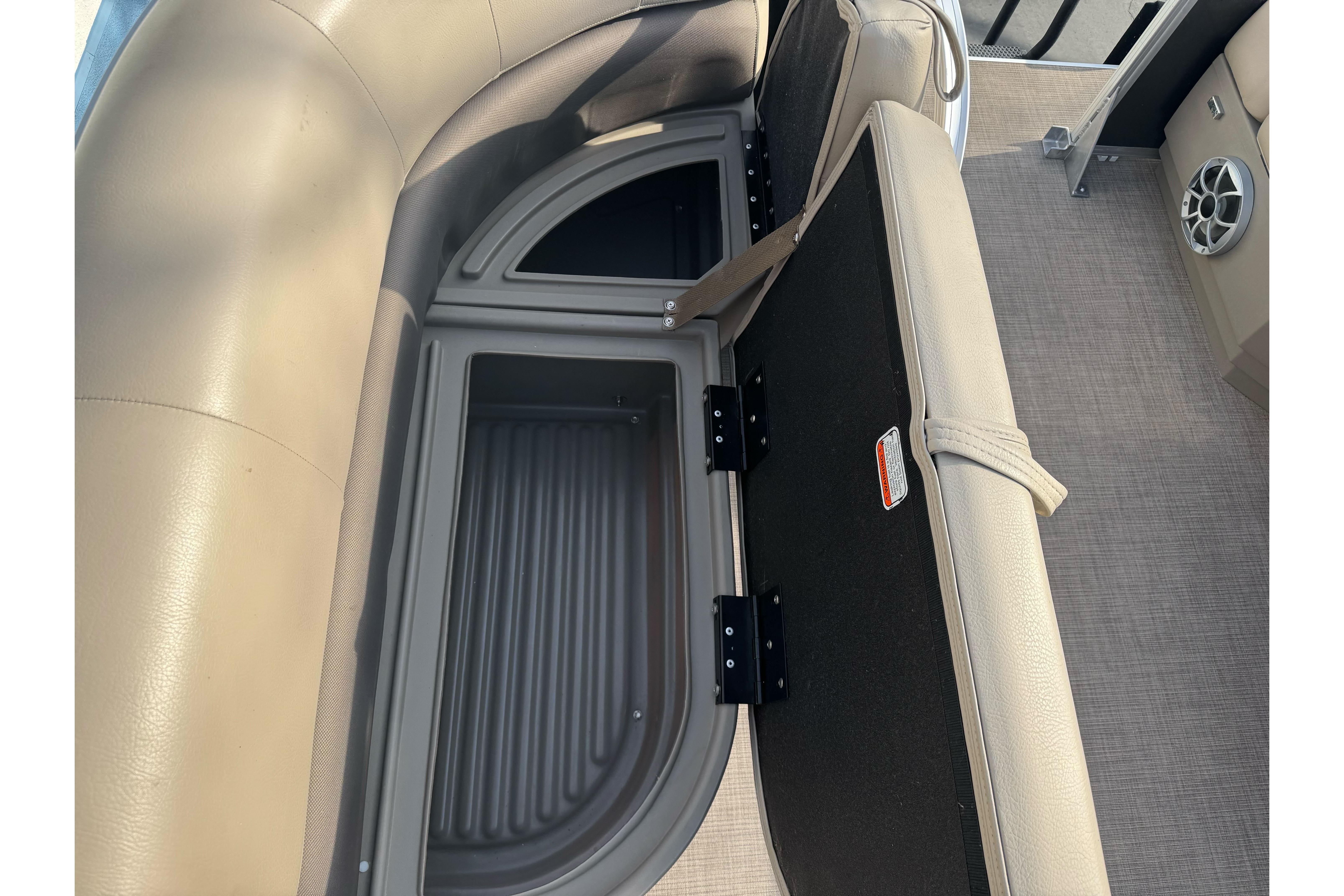 2024 Sun Tracker Party Barge 16 DLX storage compartment with beige seating and speaker.