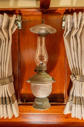Vintage oil lamp on 1939 Stephens Brothers Bridgedeck Cruiser, framed by curtains.