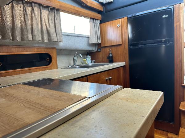 1987 Bayliner 3888 Motoryacht kitchen with wood cabinetry, countertop, and black refrigerator.