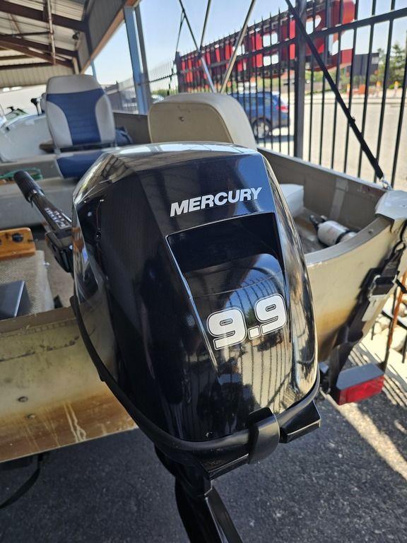 2003 Alumacraft V14 boat with Mercury 9.9 outboard motor in a parking area.