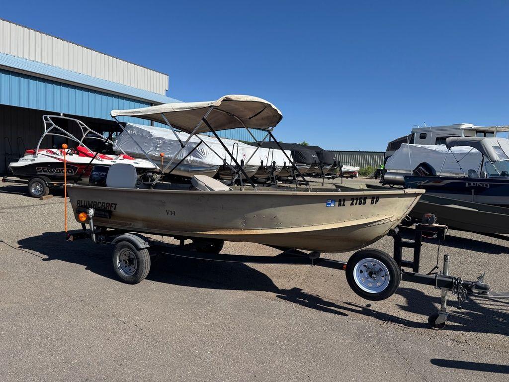 2003 Alumacraft V14 boat on trailer, parked outdoors under clear blue sky.