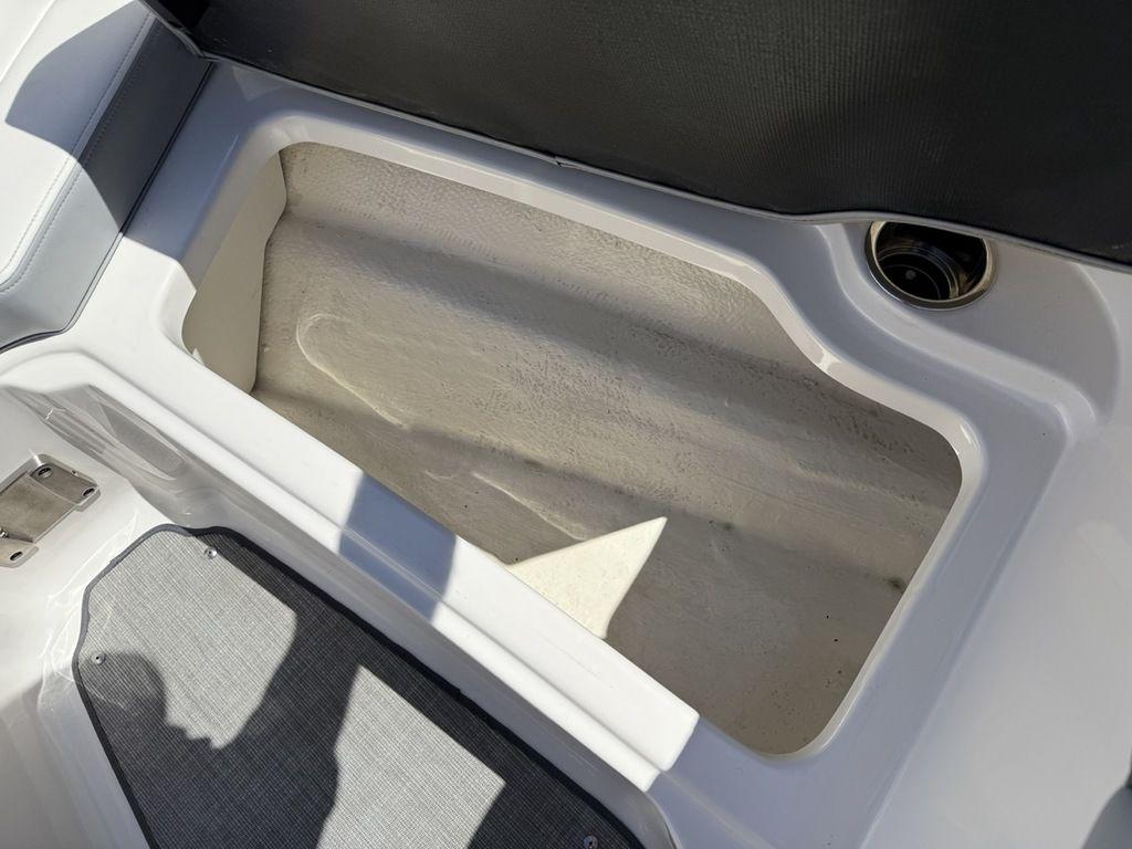 Open storage compartment in 2022 Chaparral 23 SSi boat, featuring white interior and gray flooring.