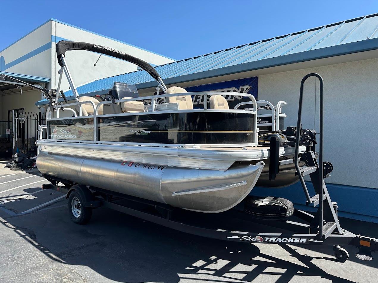 2022 Sun Tracker Bass Buggy 16 XL Select pontoon boat on trailer, parked outside.