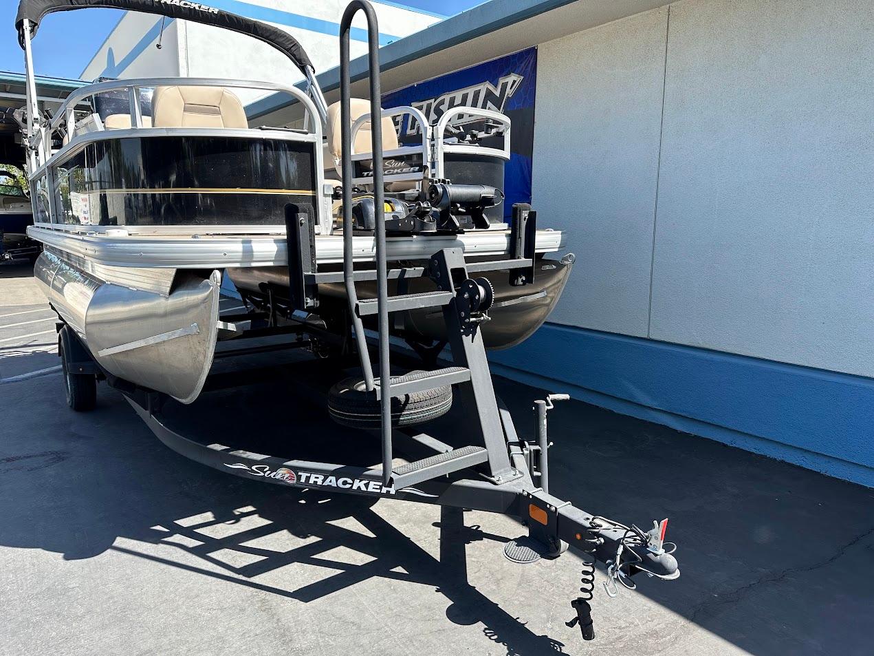 2022 Sun Tracker Bass Buggy 16 XL Select pontoon boat on trailer, parked outdoors.