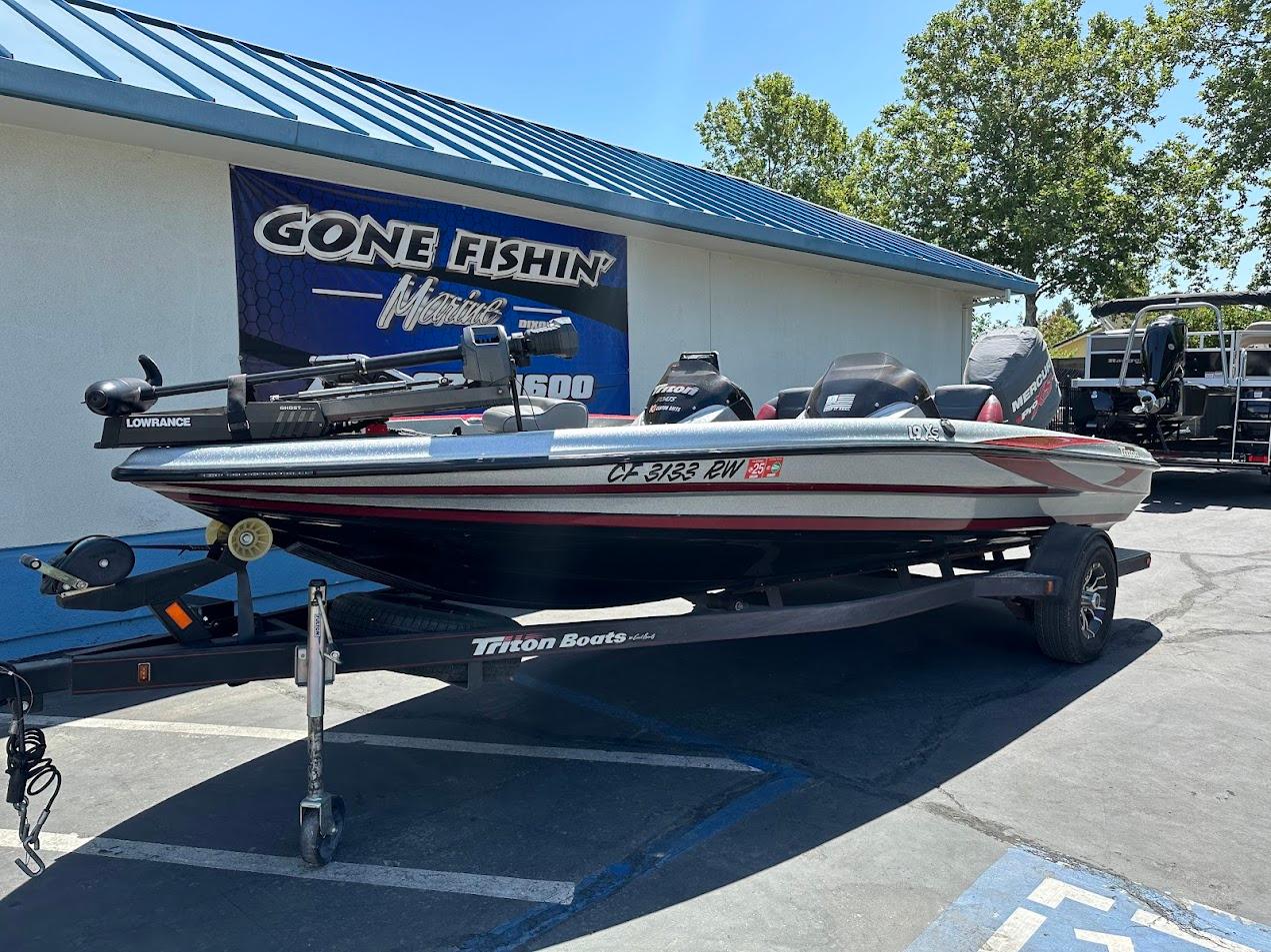 2013 Triton 19XS boat on trailer outside a fishing store, under clear blue sky.