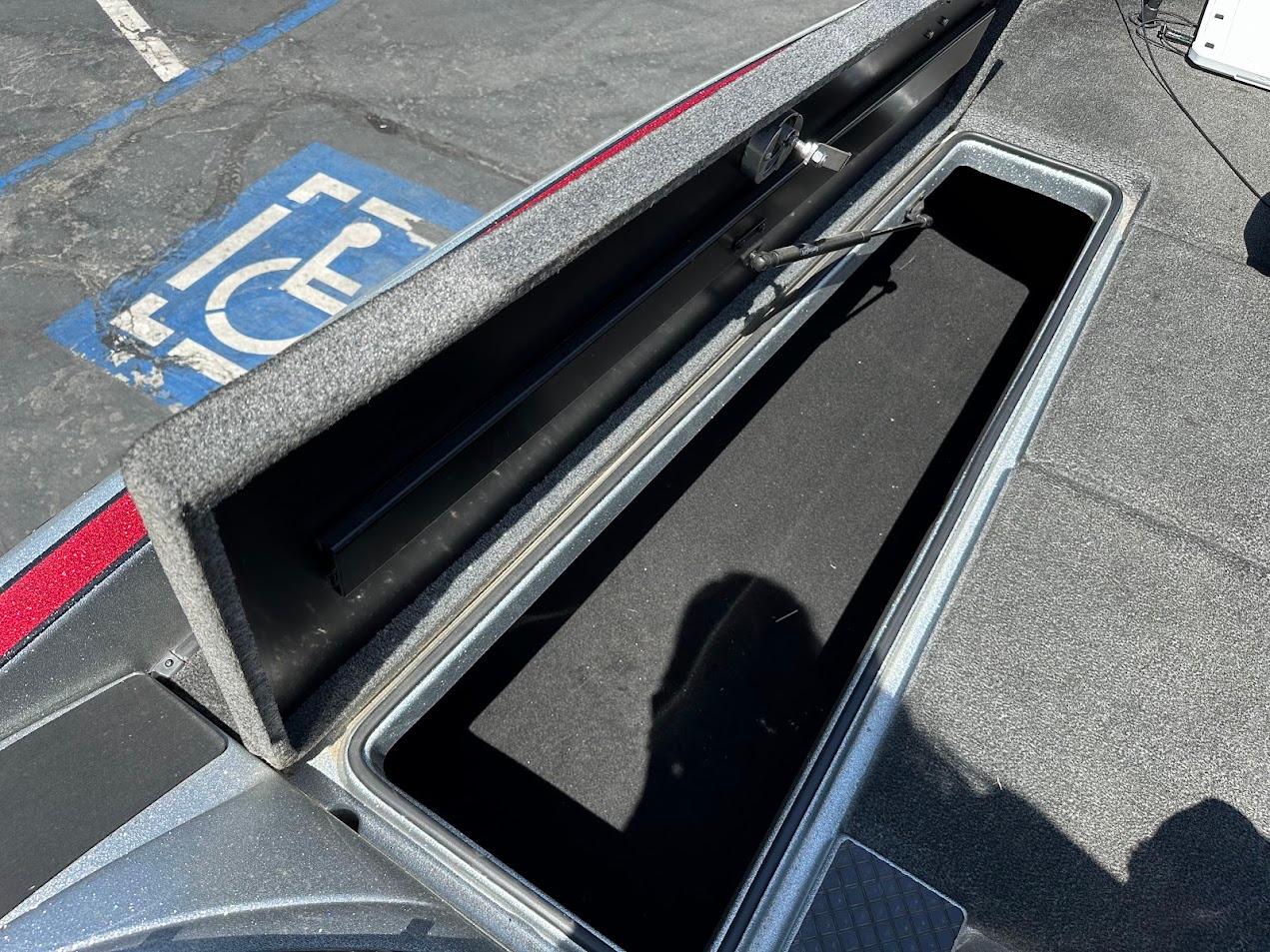 Open storage compartment on 2013 Triton 19XS boat, with shadow and parking lot background.