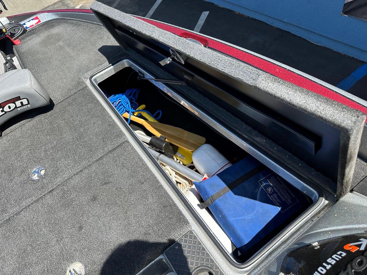 Open storage compartment on 2013 Triton 19XS boat with various items inside.