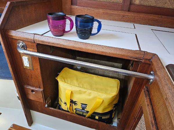 Wooden boat interior with two mugs and a yellow bag, Schock NY 36, 1984.