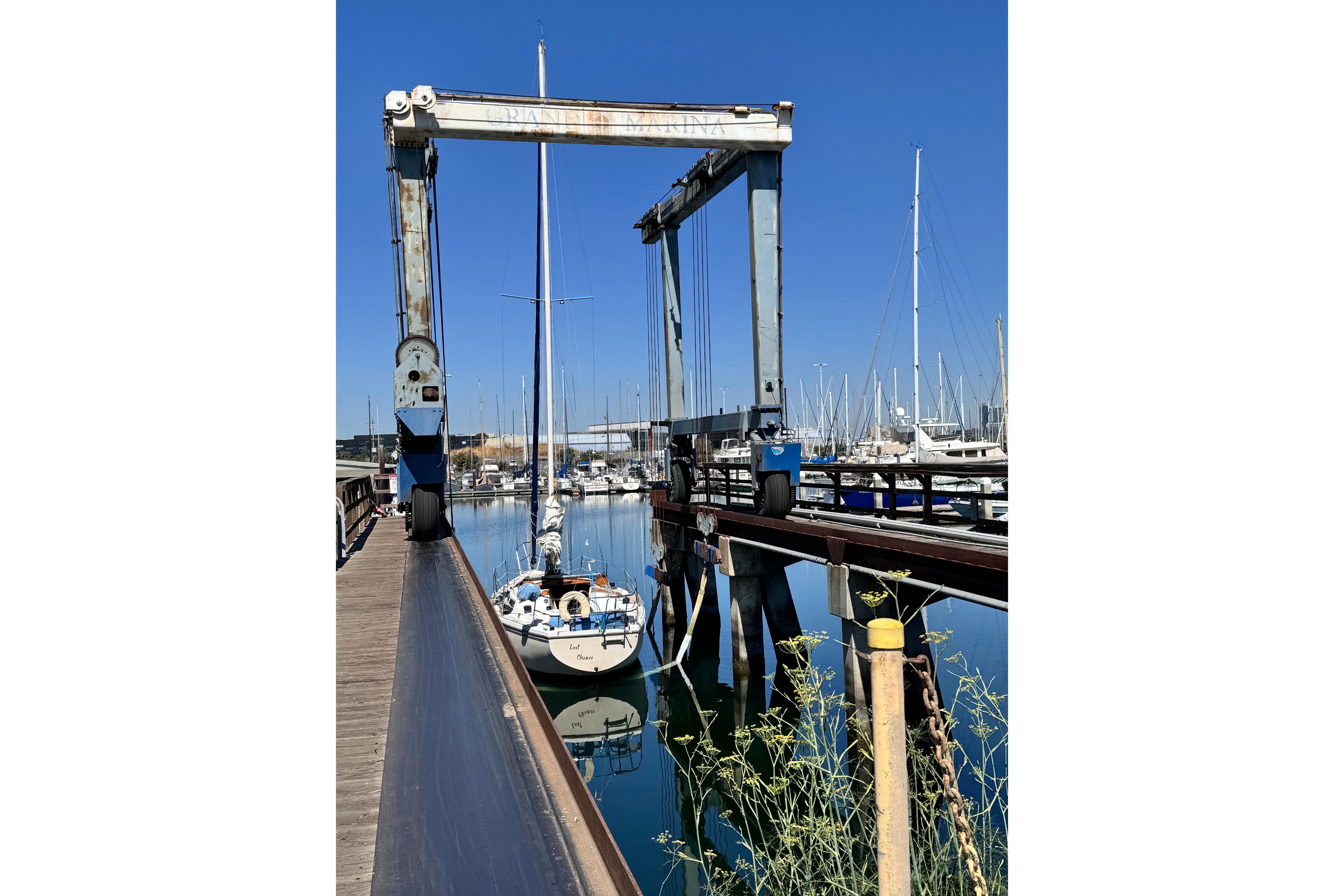 1980 Catalina 30 sailboat in marina, under boat lift, clear blue sky.