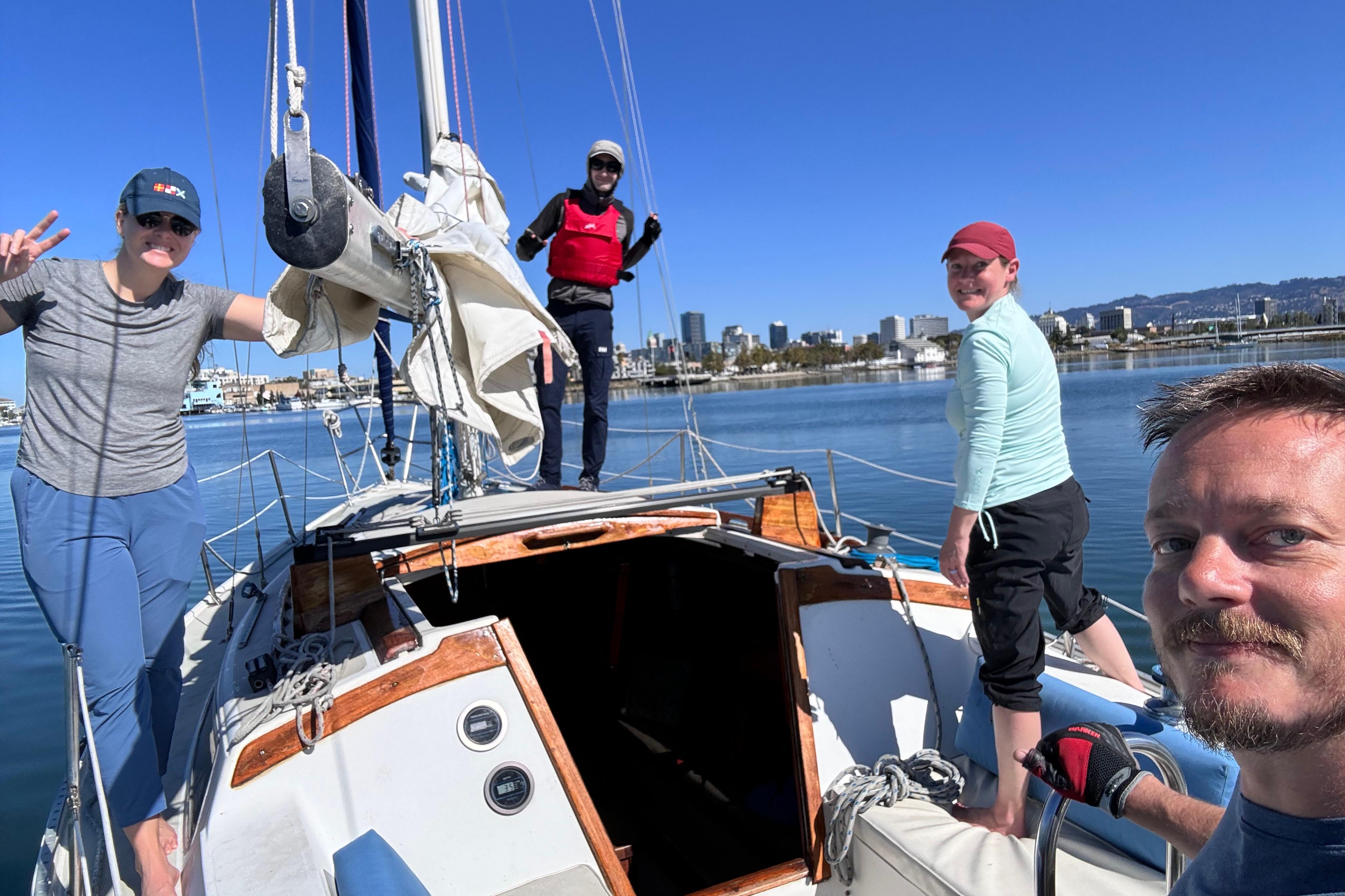 Group enjoying a sunny day on a 1980 Catalina 30 sailboat, with city skyline in background.
