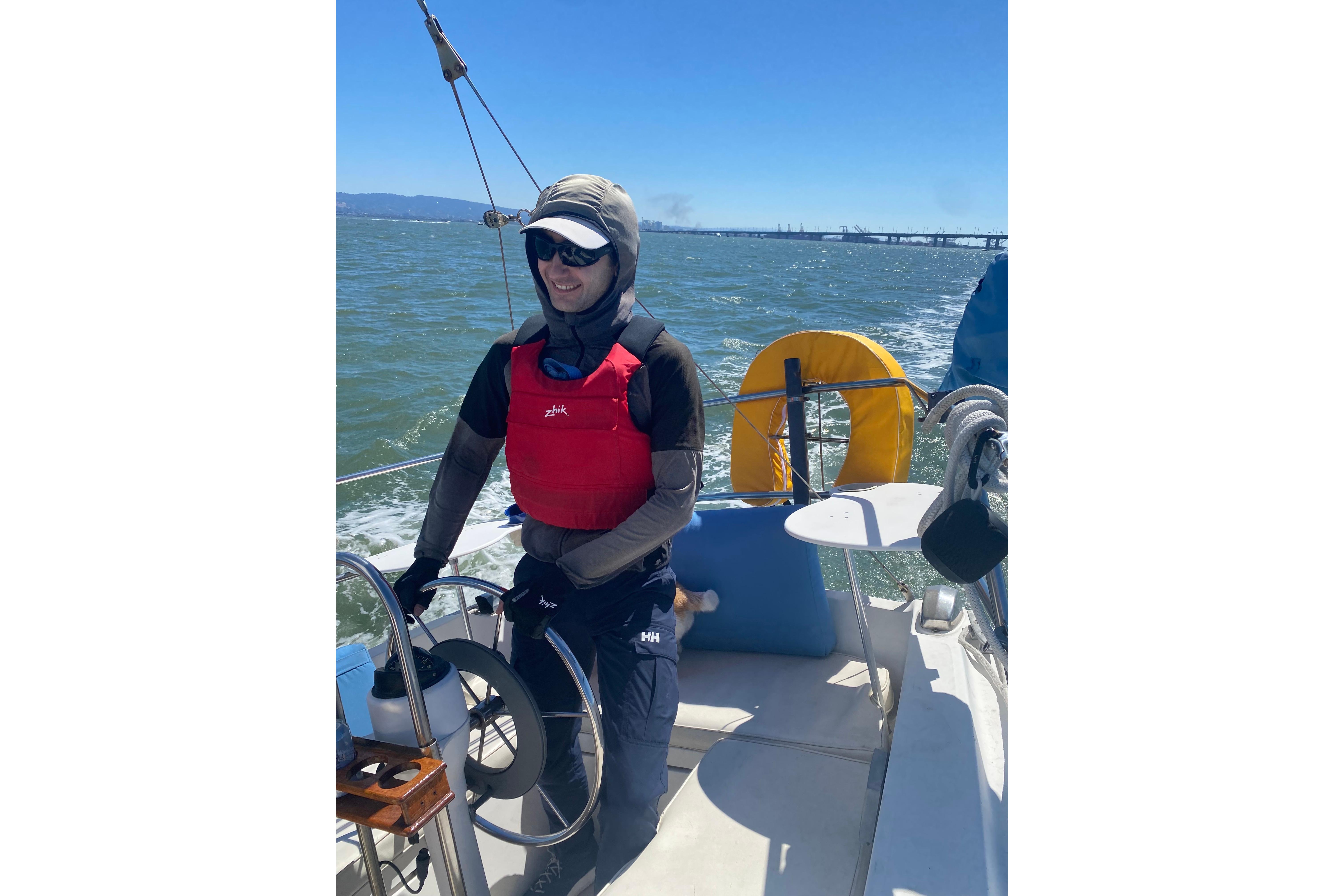 Person sailing a 1980 Catalina 30 boat on a sunny day, wearing a red life jacket.
