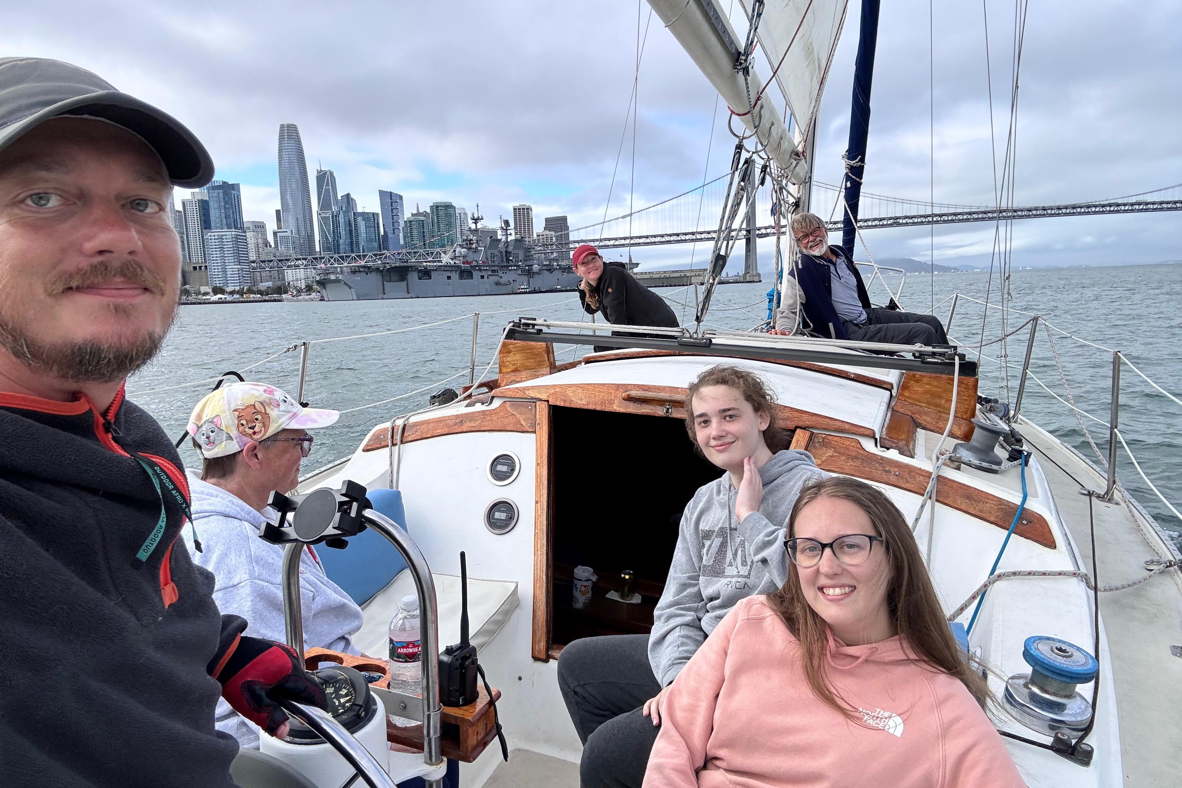 Group sailing on 1980 Catalina 30 yacht with city skyline and bridge in background.