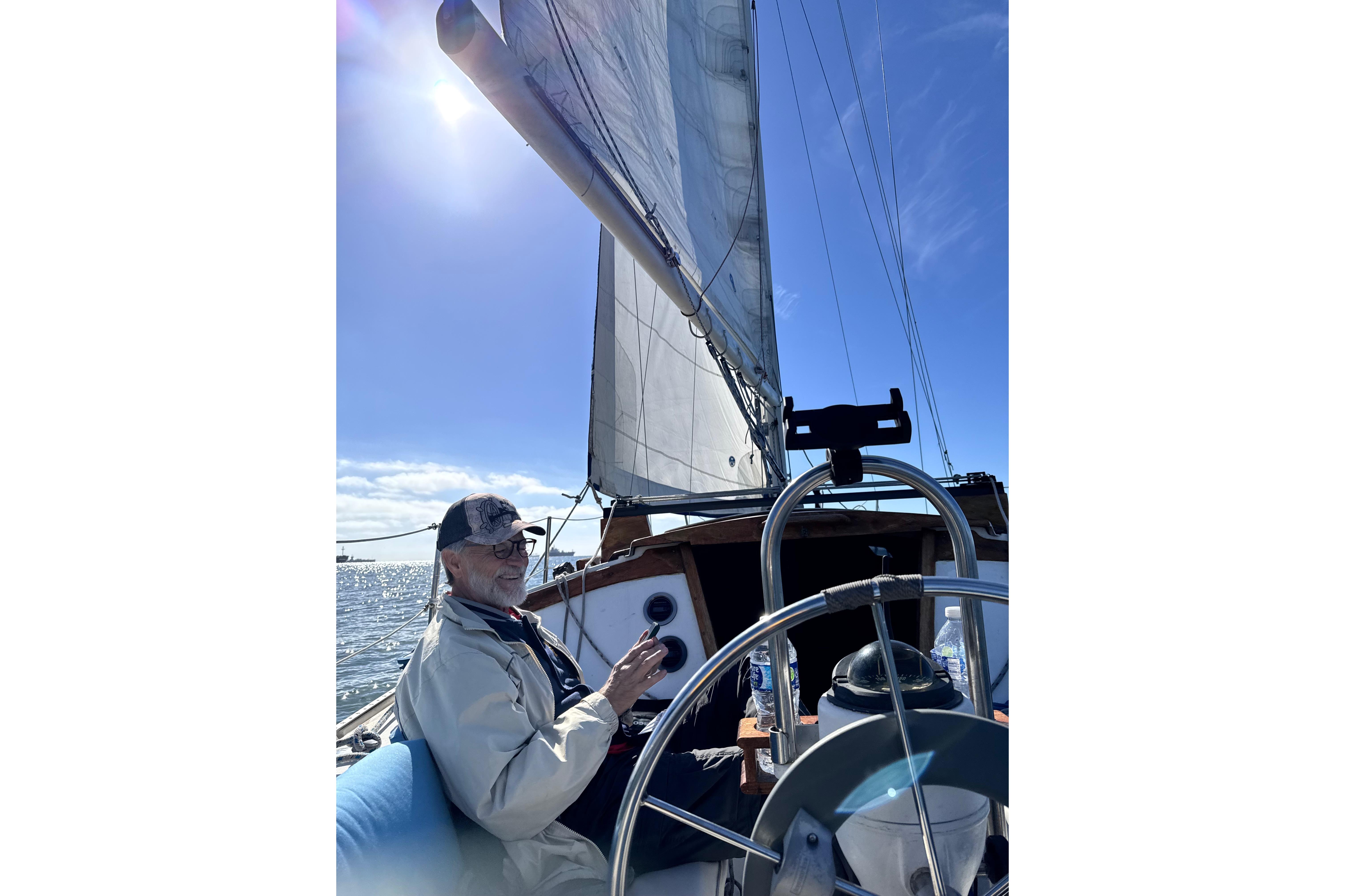 Man sailing a 1980 Catalina 30 yacht under clear blue skies.