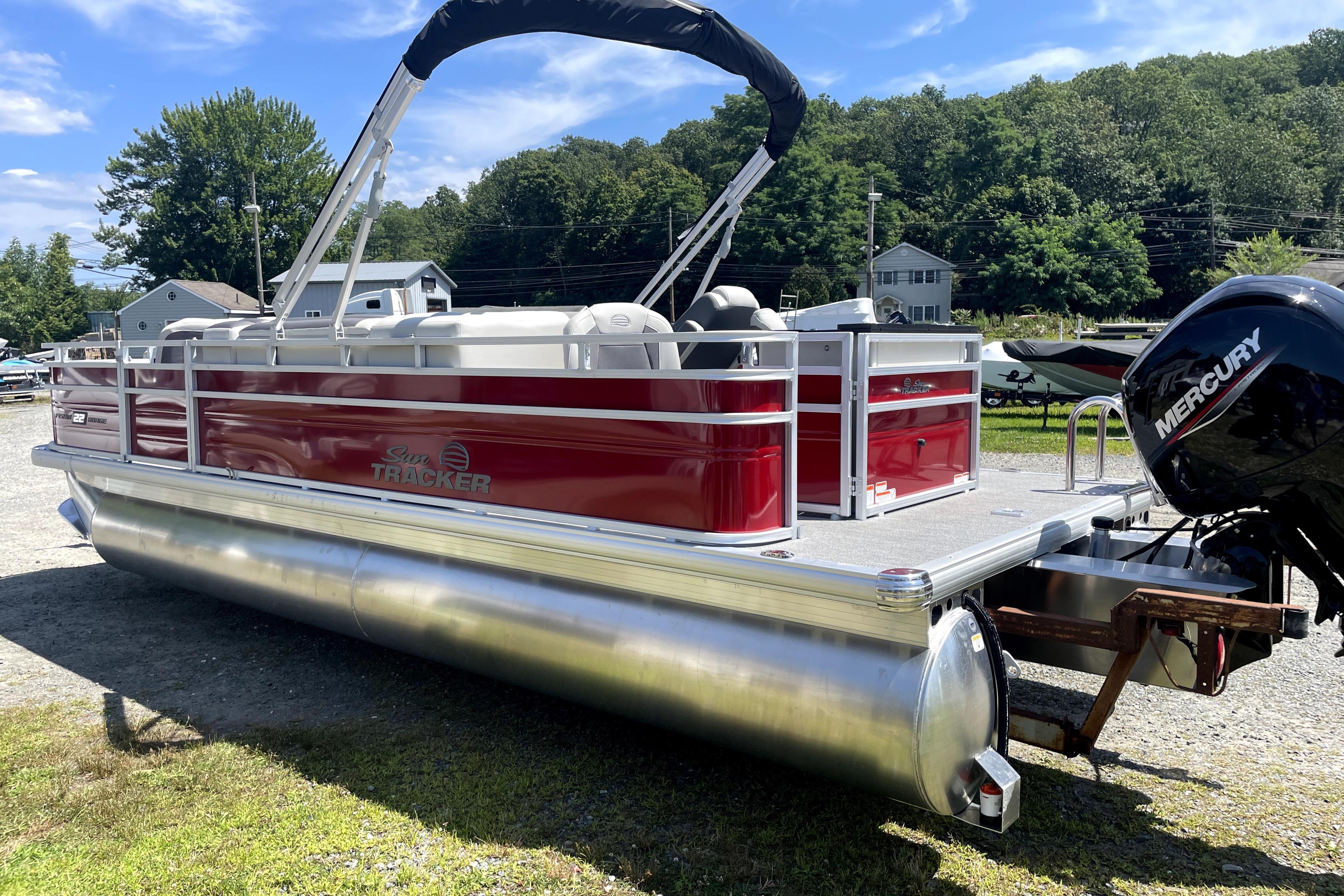 2026 Sun Tracker Fishin' Barge 22 DLX pontoon boat with Mercury engine, parked outdoors.