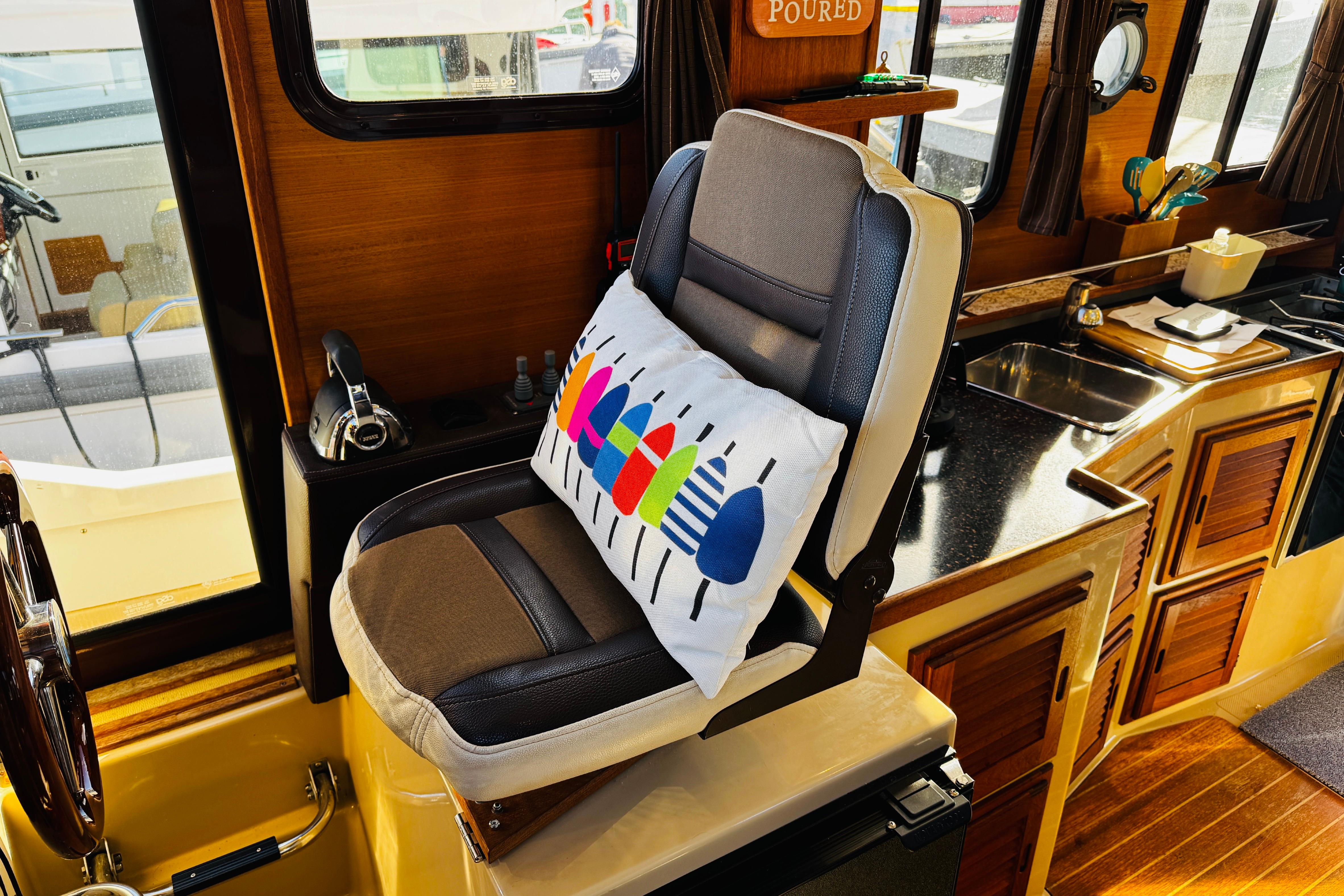 Captainu0027s chair in 2012 Ranger Tugs R-31 boat interior with colorful pillow and wooden cabinetry.