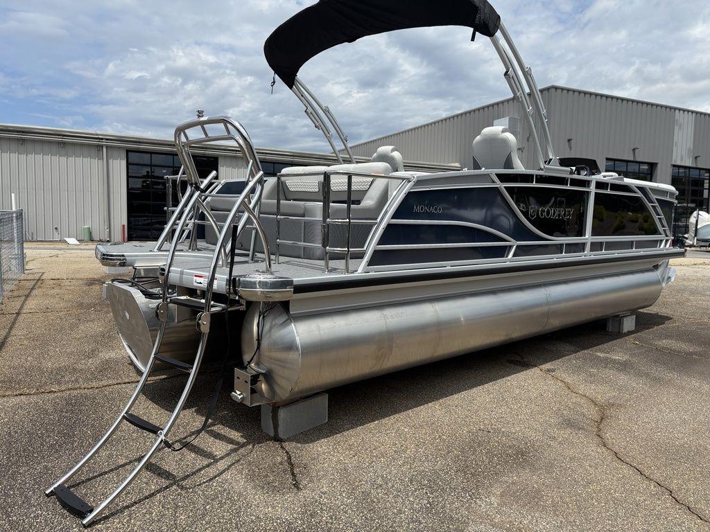 2025 Godfrey Monaco 235 DFL pontoon boat with sleek design and ladder, parked outdoors.