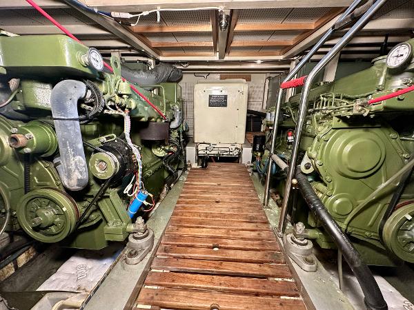 Engine room of 1982 Grand Banks Classic boat with dual green engines and wooden walkway.