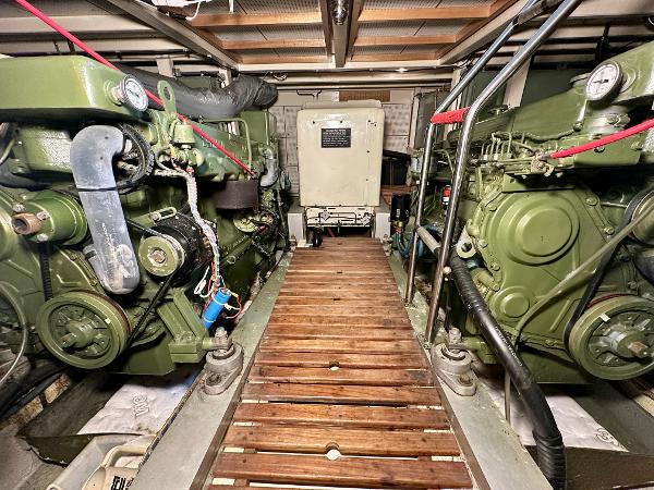 Engine room of 1982 Grand Banks Classic boat with dual green engines and wooden walkway.