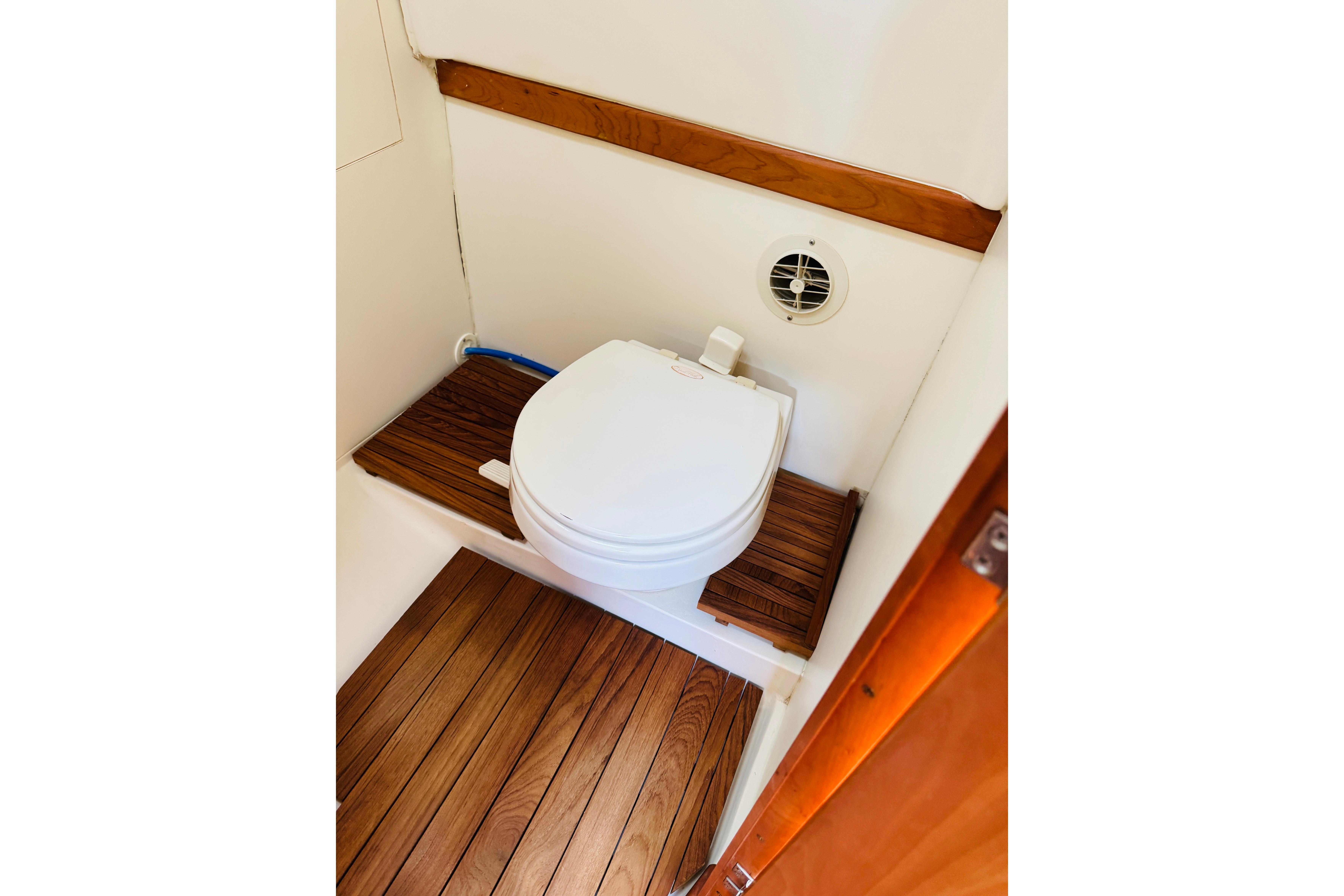 2006 Mainship Pilot 30 Sedan boat bathroom with wooden flooring and compact toilet.