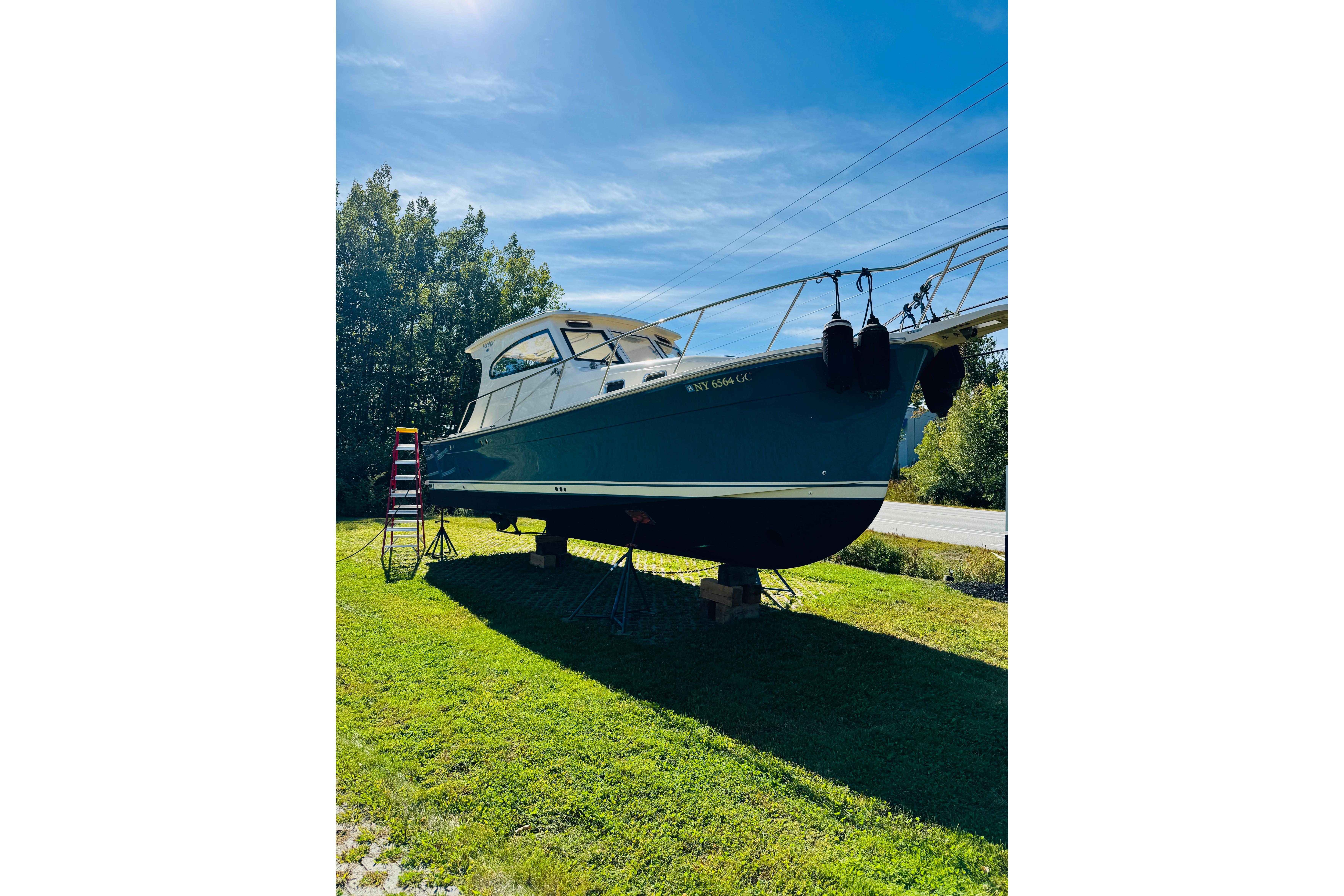 2006 Mainship Pilot 30 Sedan boat on land, sunny day, surrounded by trees.