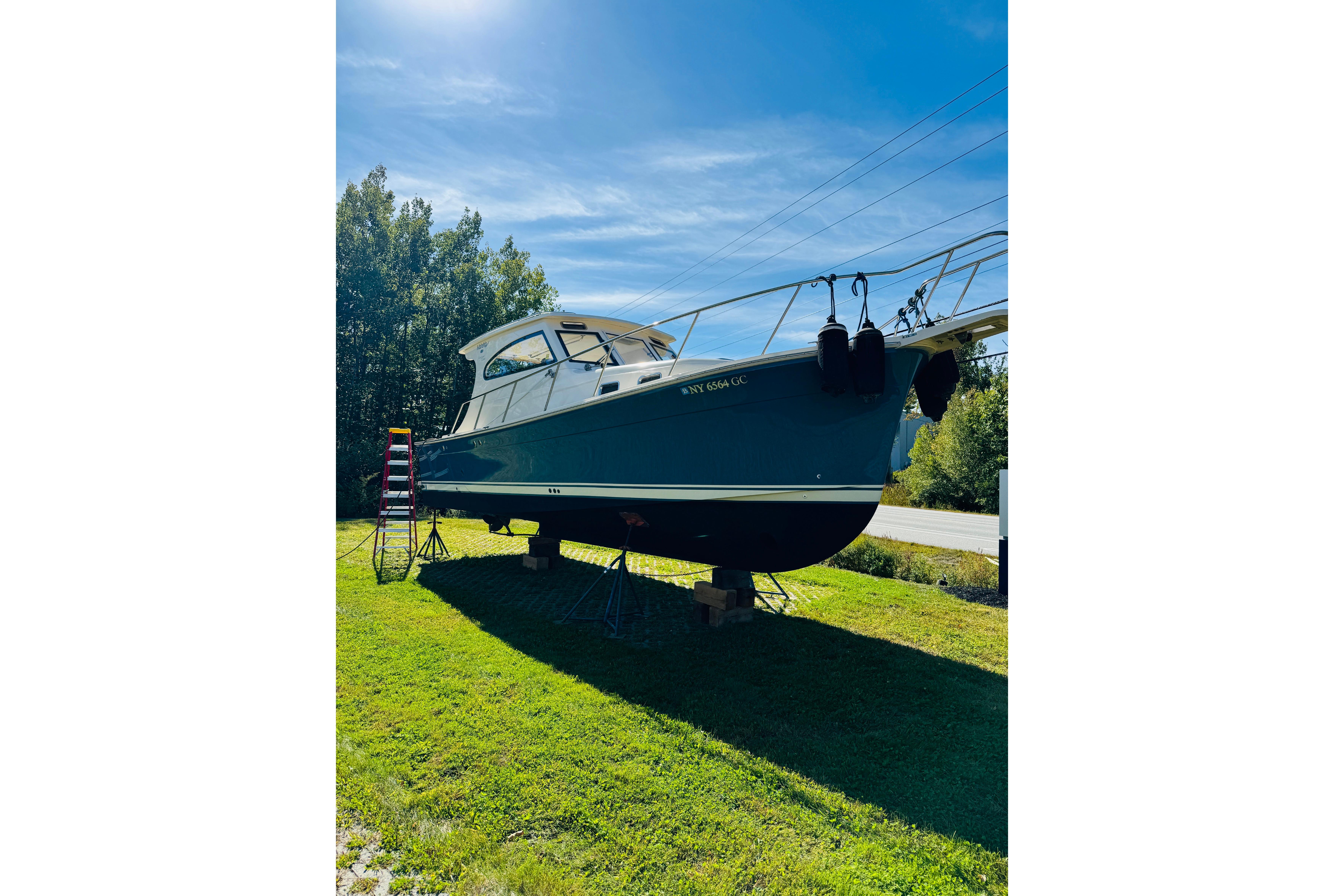 2006 Mainship Pilot 30 Sedan boat on land, sunny day, surrounded by trees.