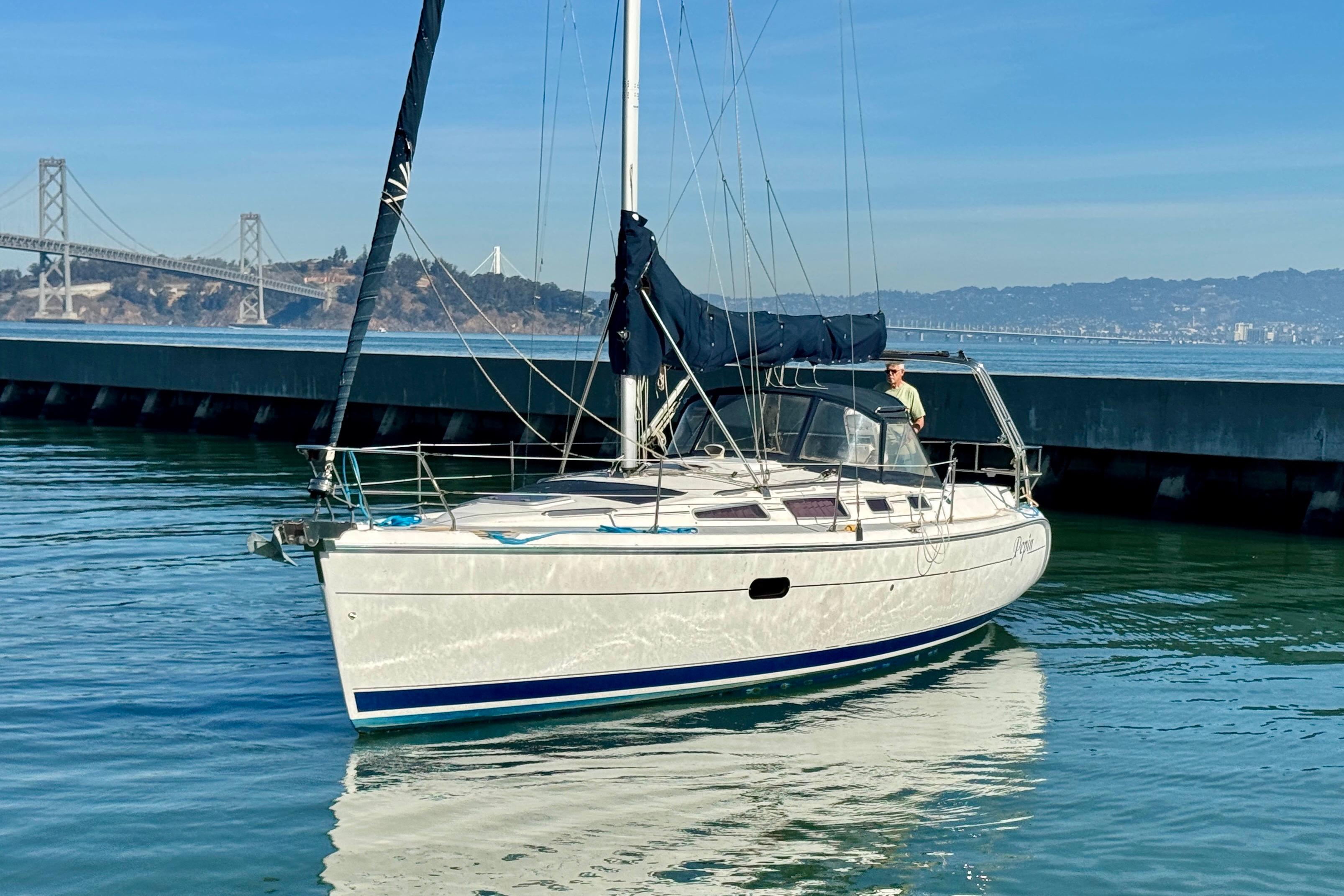 2003 Hunter 36 sailboat on calm water near a bridge, clear blue sky.