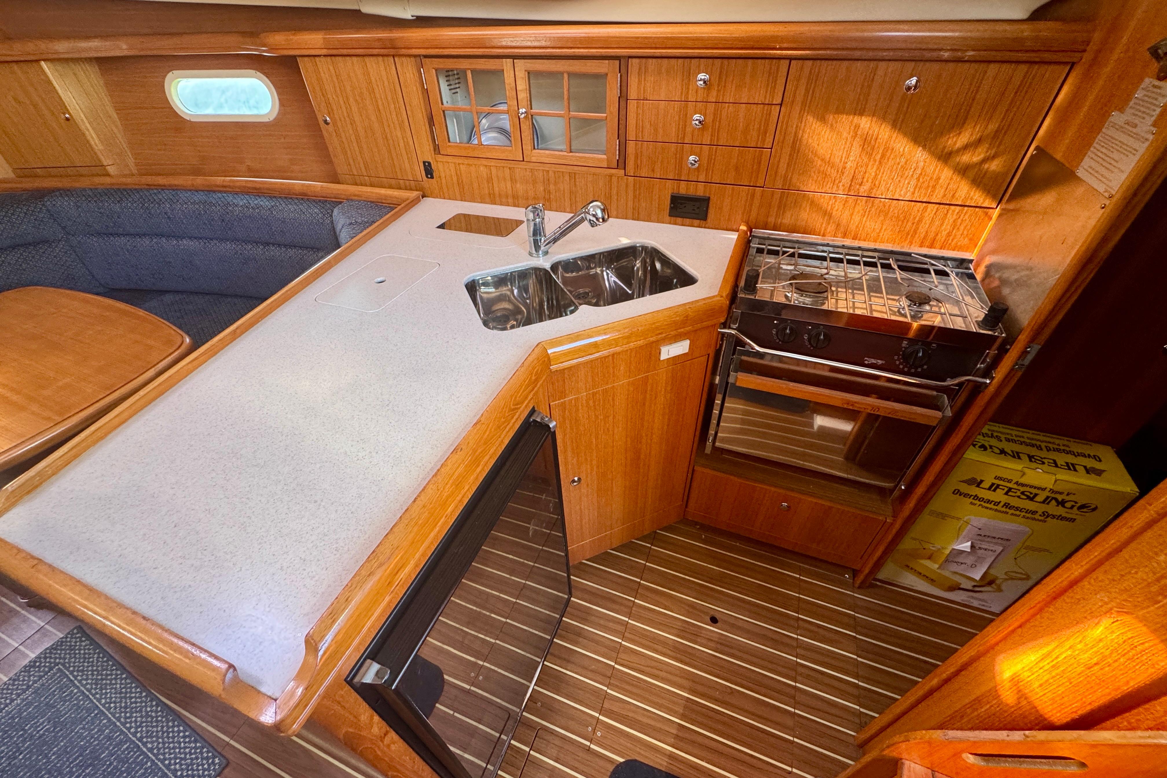 2003 Hunter 36 yacht interior kitchen with wood cabinetry, sink, stove, and seating area.